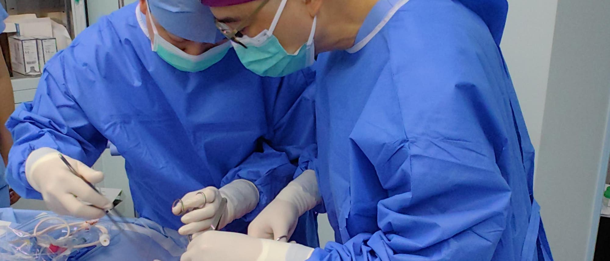 Zwei Chirurgen in blauen OP-Kitteln und Masken stehen über einem Operationstisch, auf dem chirurgische Instrumente und das Operationsfeld zu sehen sind.