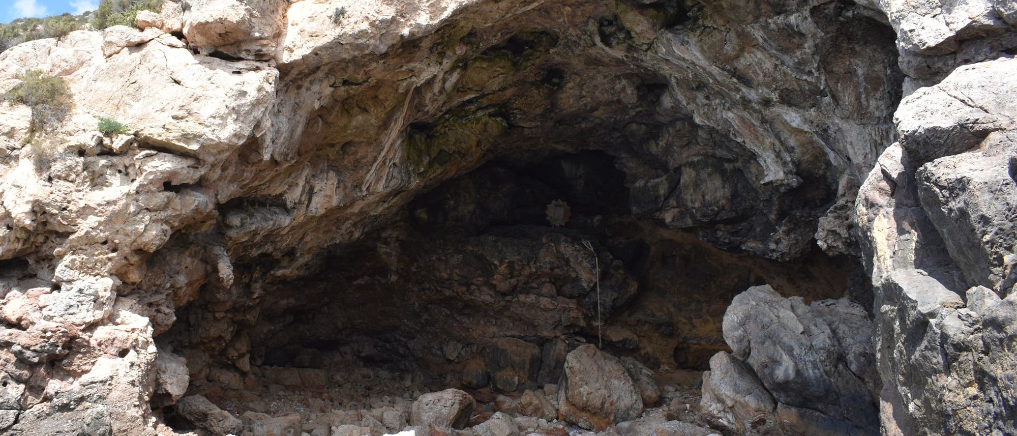 Eine natürliche Felsgrotte an einer Küste, umgeben von rauen, steinigen Klippen. Die Höhle öffnet sich zum Meer, das im Vordergrund sichtbar ist, mit klarem, türkisfarbenem Wasser. Vegetation wächst spärlich auf den Felsen oberhalb der Höhle. Der Himmel ist teilweise bewölkt. Eine natürliche Felsgrotte an einer Küste, umgeben von rauen, steinigen Klippen. Die Höhle öffnet sich zum Meer, das im Vordergrund sichtbar ist, mit klarem, türkisfarbenem Wasser. Vegetation wächst spärlich auf den Felsen oberhalb der Höhle. Der Himmel ist teilweise bewölkt.