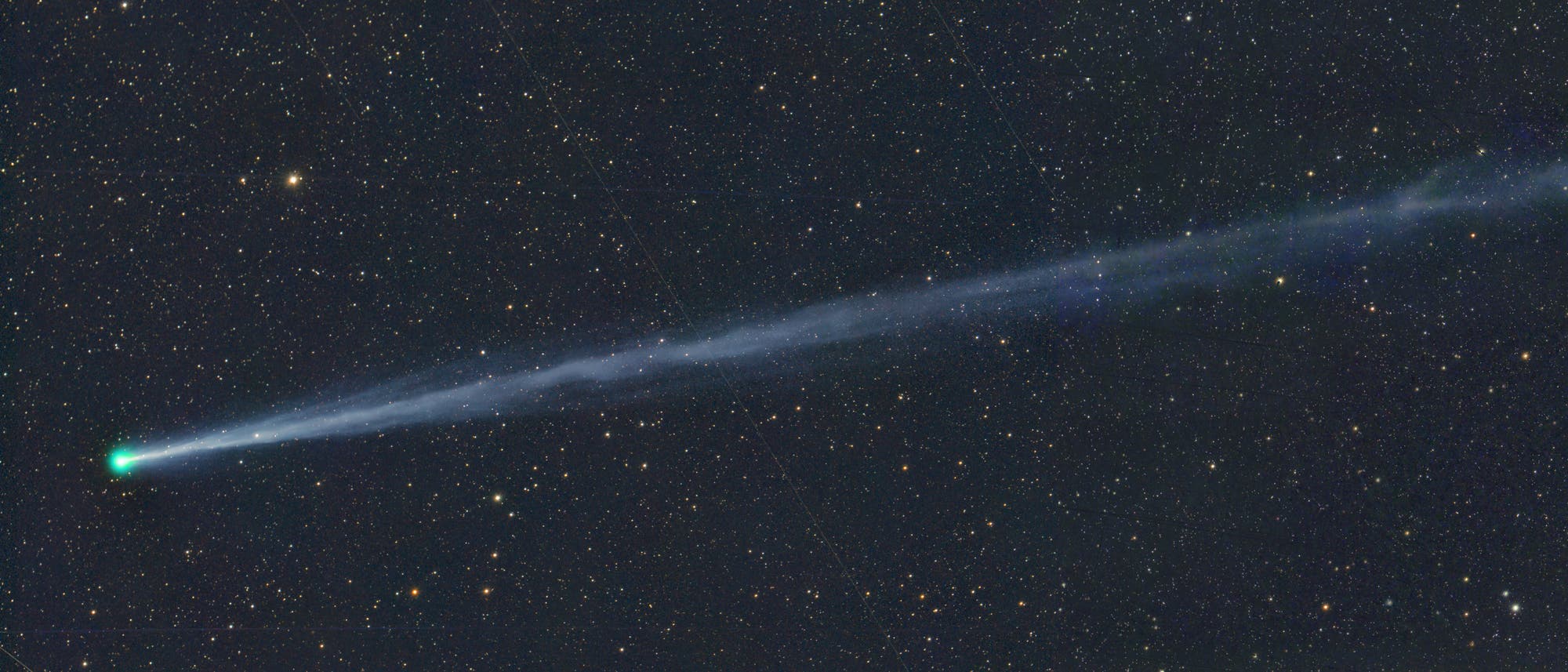 Ein Komet mit einem leuchtend gr&uuml;nen Kopf und einem langen, bl&auml;ulichen Schweif zieht durch ein sternen&uuml;bers&auml;tes Universum. Der Schweif erstreckt sich diagonal &uuml;ber das Bild und hebt sich gegen den dunklen Hintergrund des Weltraums ab. Zahlreiche Sterne unterschiedlicher Helligkeit sind im Hintergrund sichtbar.