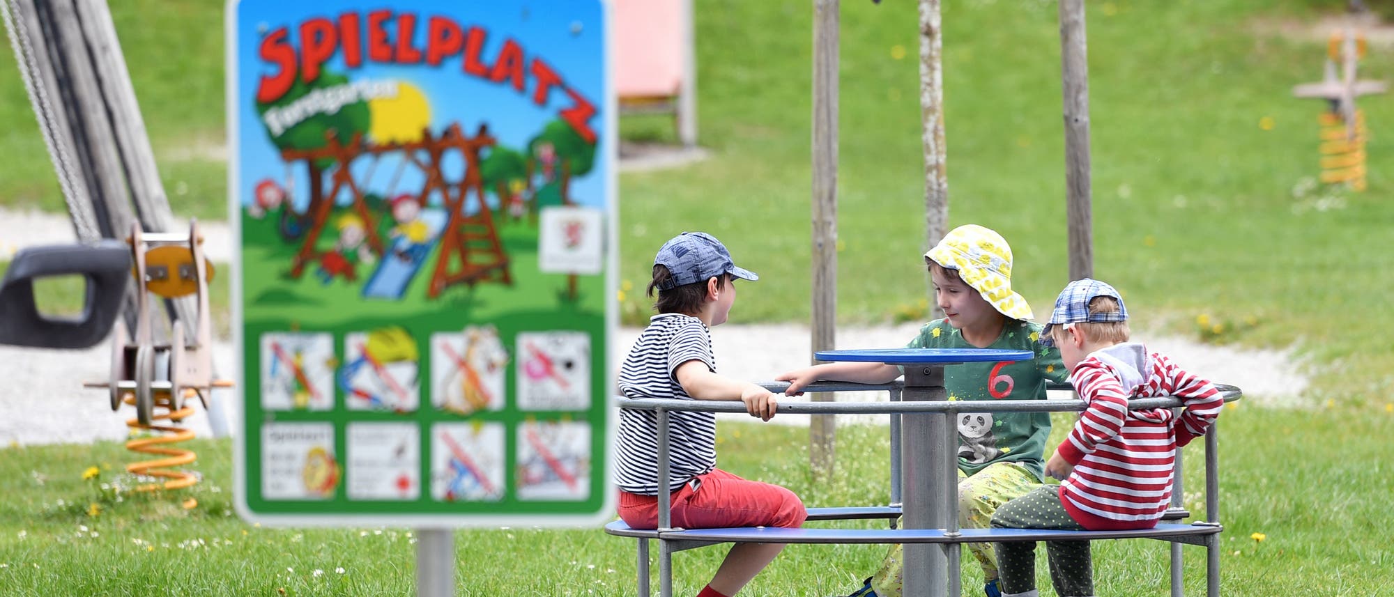Kinder sitzen auf einem Spielplatz in einem Karussel.