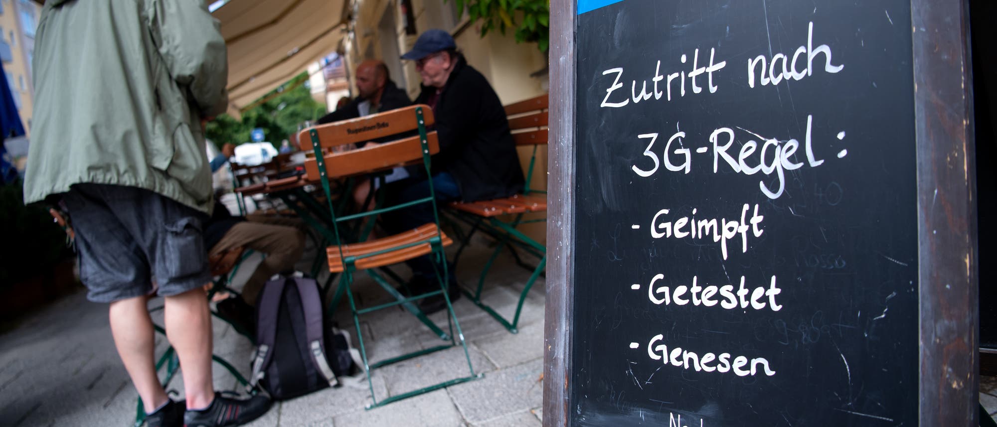 Ein Aufstellschild mit Hinweis auf die 3G-Regeln, im Hintergrund der Außenbereich eines Cafés.