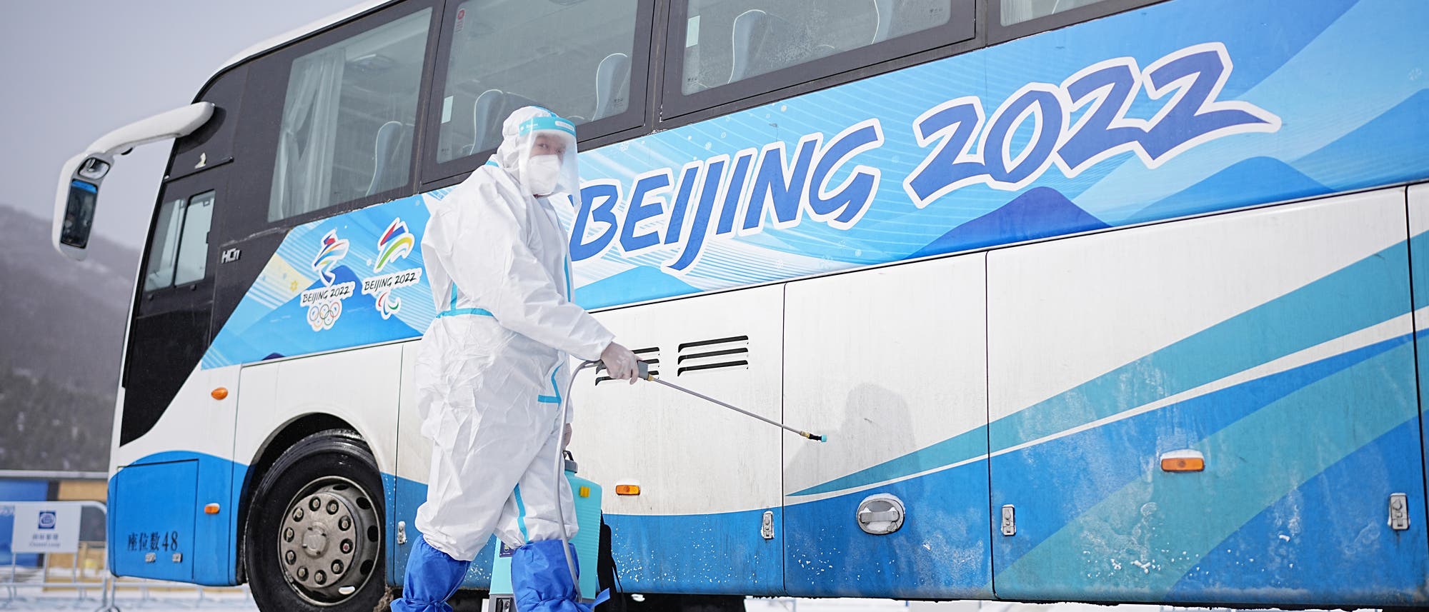Ein Arbeiter in weißer Schutzkleidung desinfiziert einen Shuttlebus für die olympischen Spiele 2022.