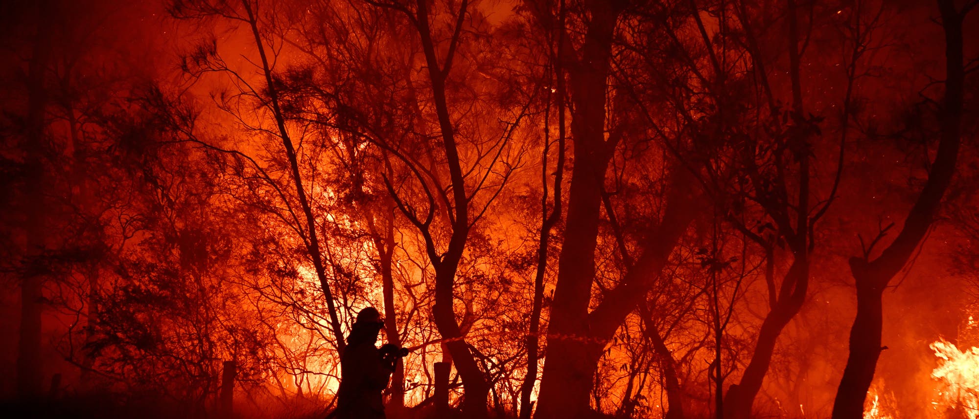 Dunkle Silhouette eines Feuerwehrmannes, der versucht, einen Waldbrand zu löschen