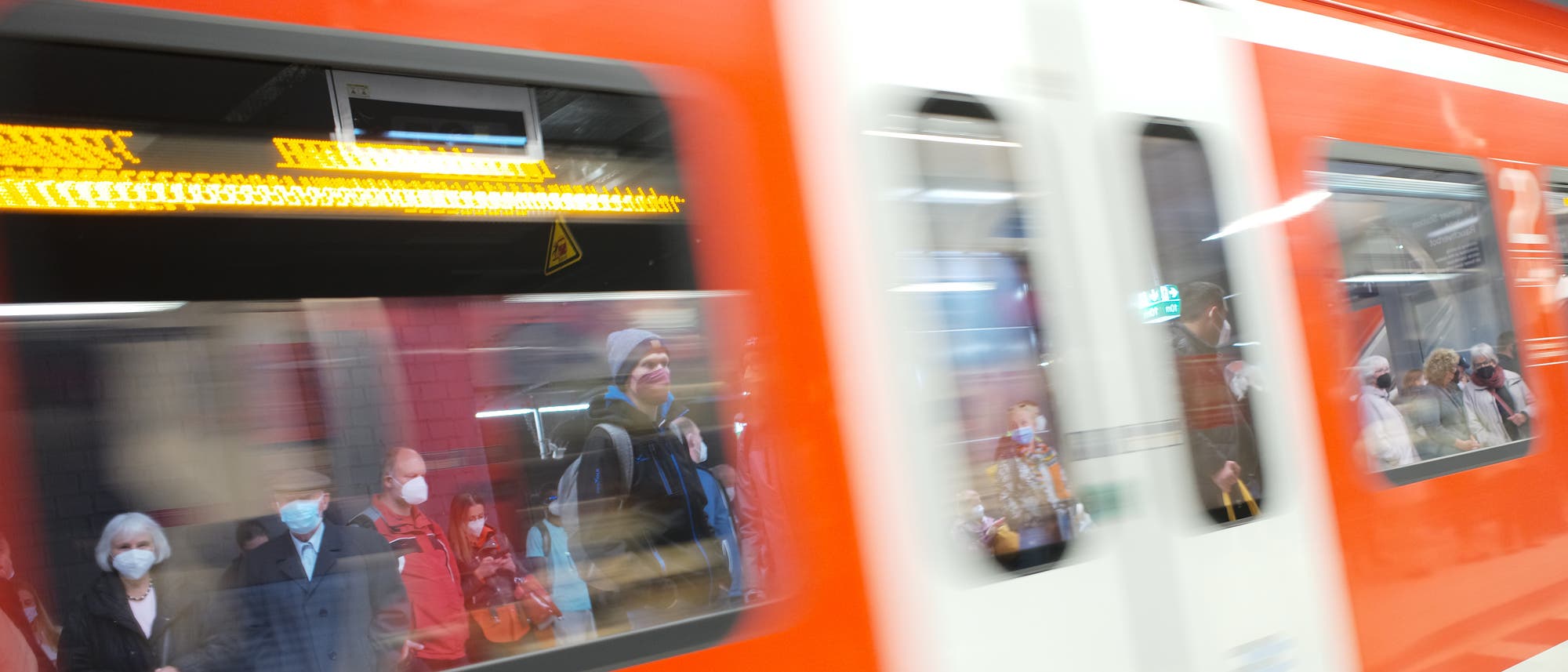 Reisende mit Mundschutzmaske warten auf einfahrende S-Bahn.