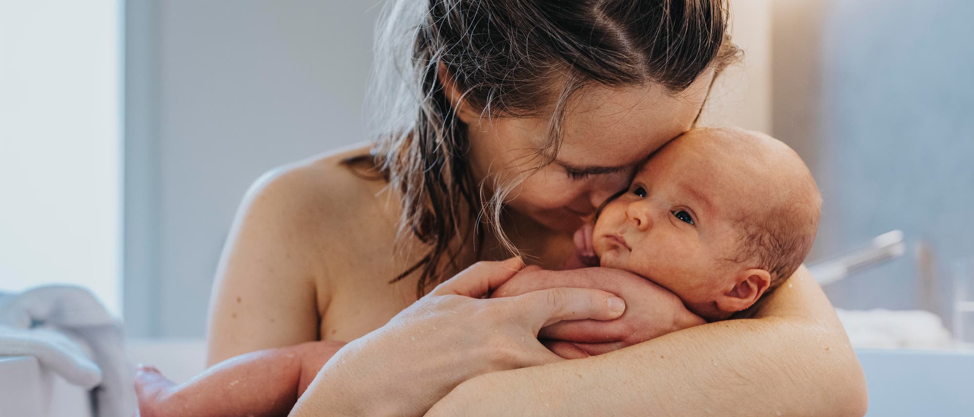 Eine Mutter sitzt in einer Badewanne und hält ihr Baby fest im Arm und kuschelt mit ihm