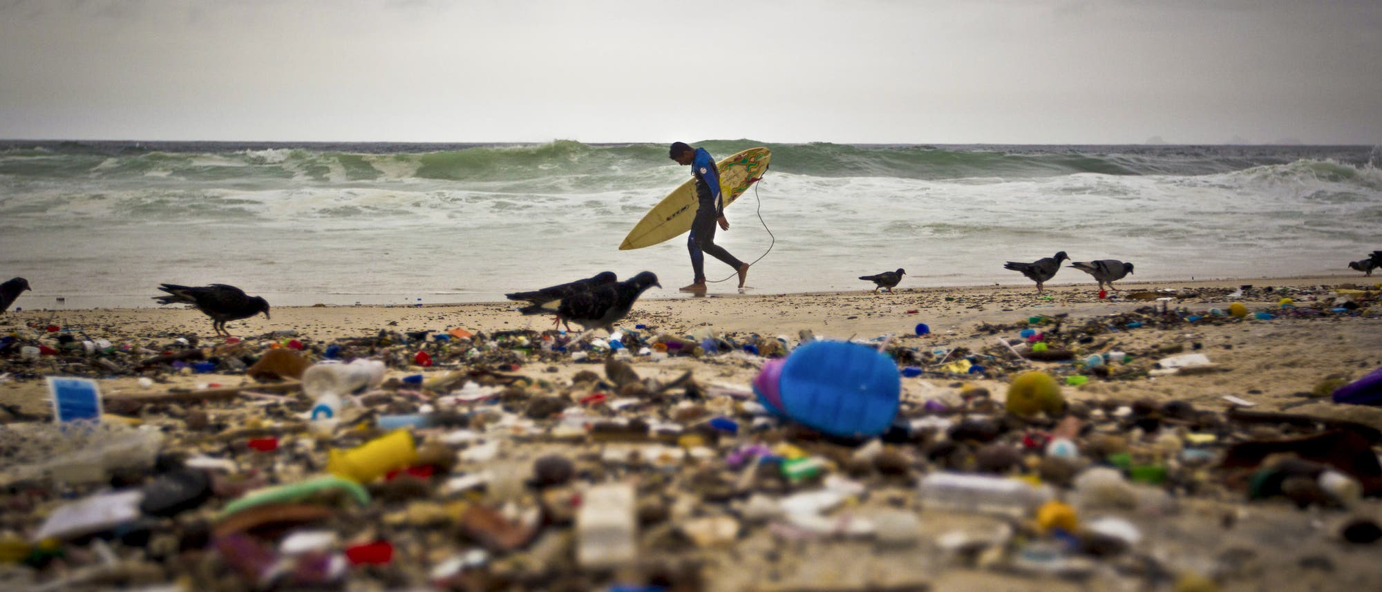 Ein Surfer steht am Strand vor einer Kulisse aus Müll