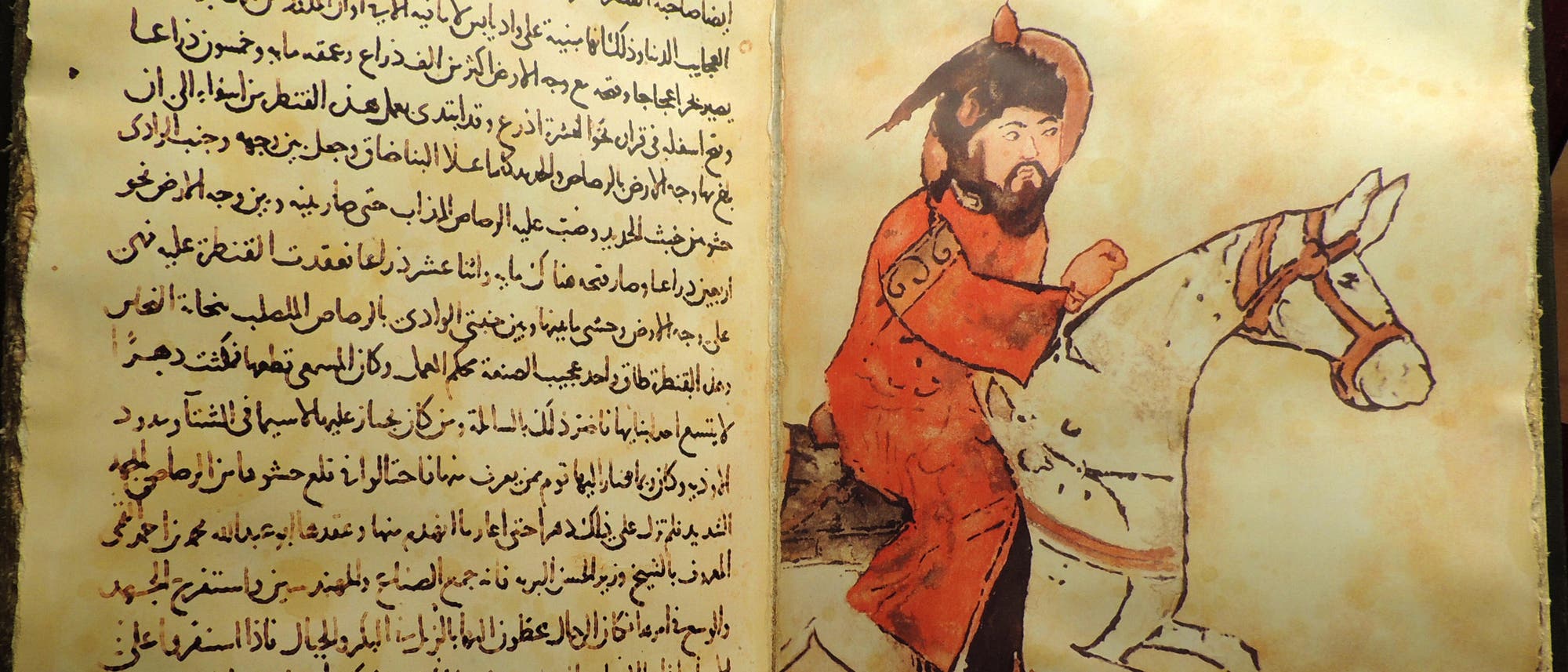 Eine antike Buchseite mit arabischer Schrift auf der linken Seite und einer Illustration auf der rechten Seite. Die Illustration zeigt eine Person in roter Kleidung, die auf einem weißen Pferd reitet. Die Seite wirkt alt und vergilbt, was auf ein historisches Dokument hinweist. Eine antike Buchseite mit arabischer Schrift auf der linken Seite und einer Illustration auf der rechten Seite. Die Illustration zeigt eine Person in roter Kleidung, die auf einem weißen Pferd reitet. Die Seite wirkt alt und vergilbt, was auf ein historisches Dokument hinweist.