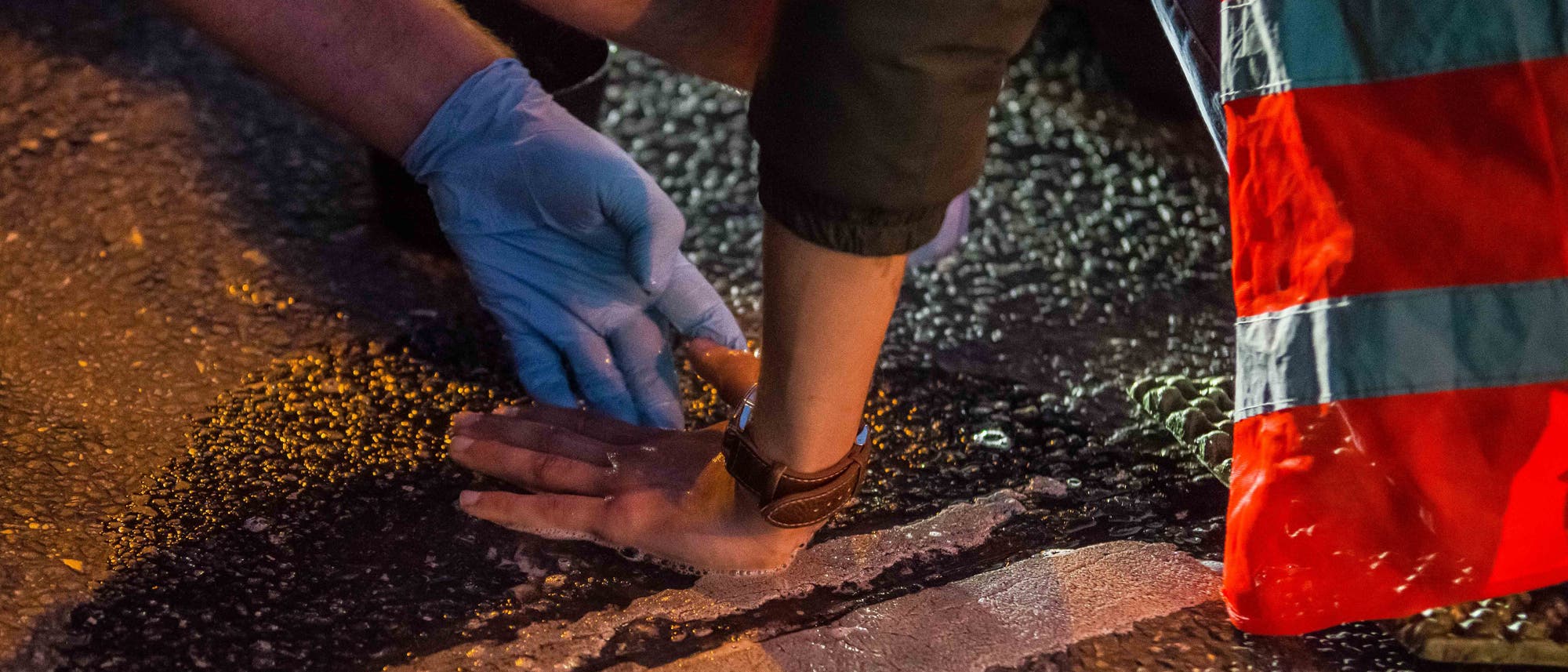 Hand eines Klimaaktivisten, der sich auf die Straße geklebt hat. Einsatzkräfte versuchen, die Hand von der Straße abzulösen. 