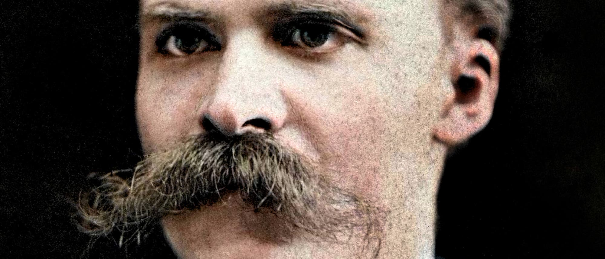 Ein Porträtfoto eines Mannes mit einem markanten Schnurrbart. Er trägt einen Anzug mit Hemd und Fliege. Der Hintergrund ist dunkel, wodurch der Fokus auf das Gesicht des Mannes gelegt wird.