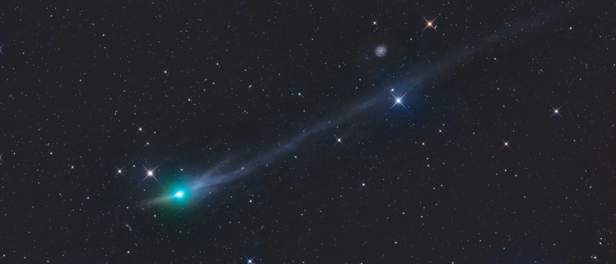 Ein astronomisches Bild zeigt den Kometen 3I/ATLAS mit einem leuchtend gr&uuml;nen Kern und einem langen, schmalen Schweif, der sich nach rechts erstreckt. Der Hintergrund ist mit zahlreichen Sternen &uuml;bers&auml;t. Der Komet hebt sich durch seine Farbe und Helligkeit von den umliegenden Sternen ab. Der Schweif des Kometen ist leicht gebogen und zeigt eine feine Struktur. 