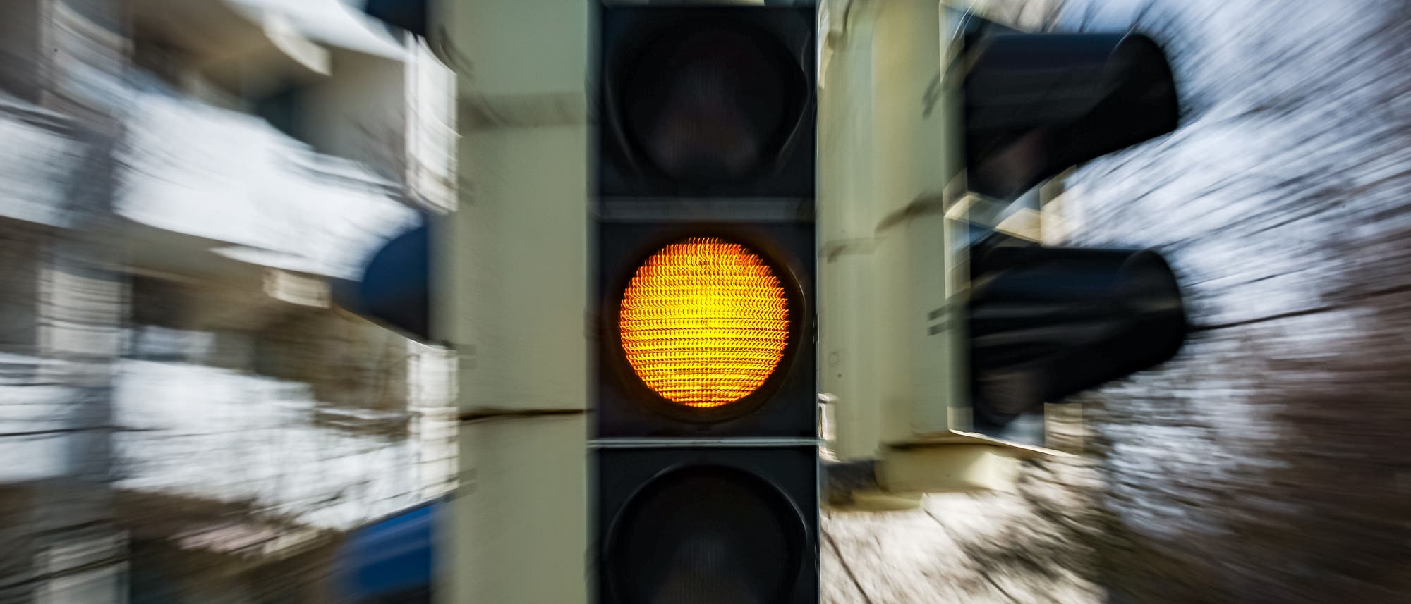 Eine Verkehrsampel mit gelbem Licht, das leuchtet, signalisiert den Fahrern, sich auf das Anhalten vorzubereiten. Die Umgebung ist verschwommen, was auf Bewegung oder Geschwindigkeit hindeutet.