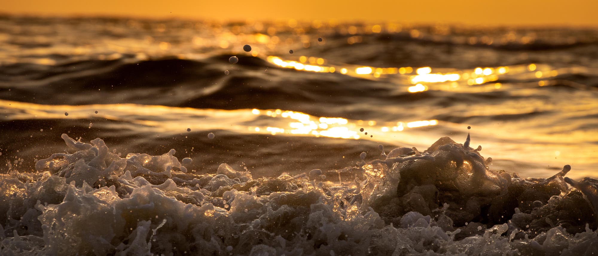 Dunkle Wellen branden im goldenen Abendlicht an den Strand