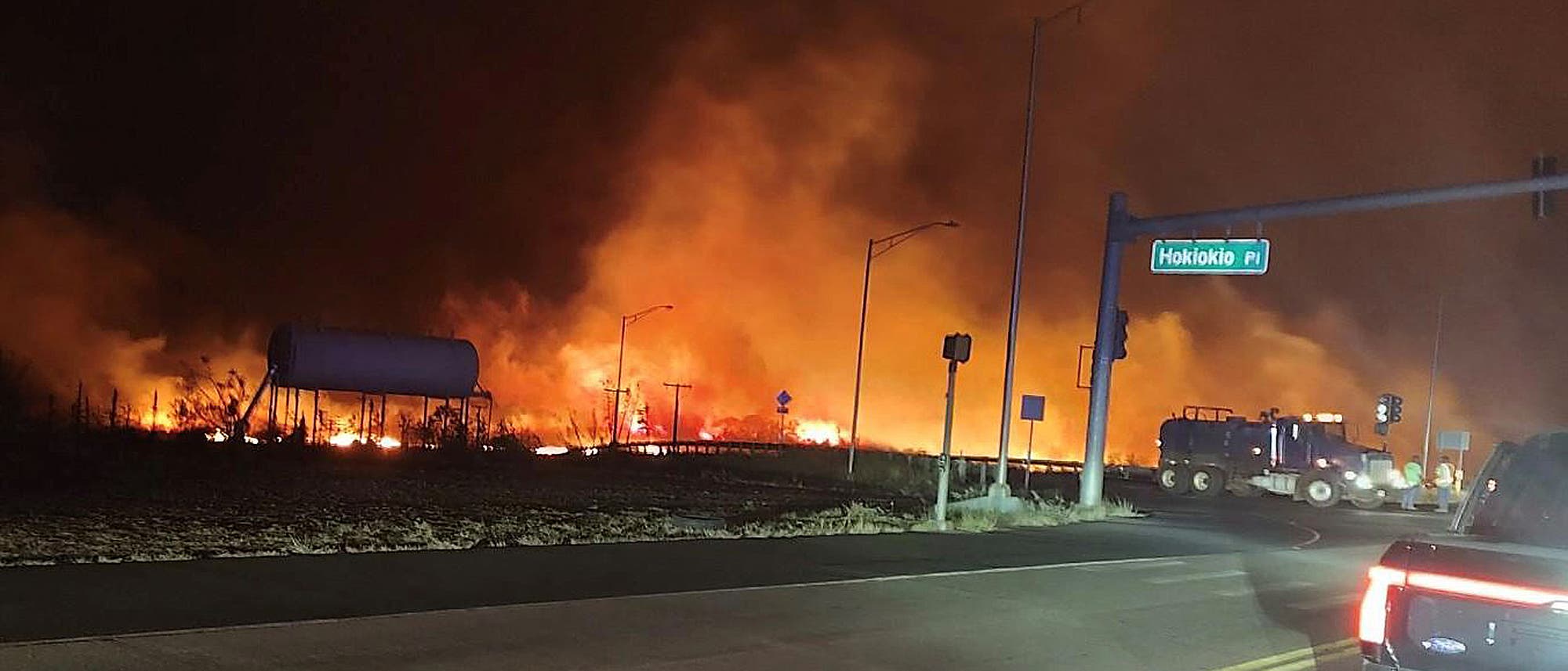 Waldbrand nahe einer Straße auf der Insel Maui, davor ein Feuerwehrauto bei Nacht