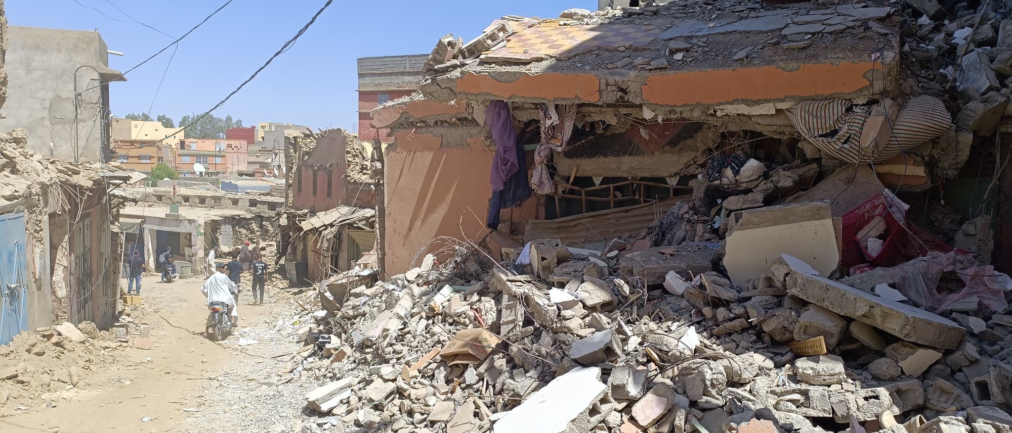 Eine Straße in einer mediterran anmutenden Stadt mit vielen teilweise zerstörten Gebäuden und Trümmern.