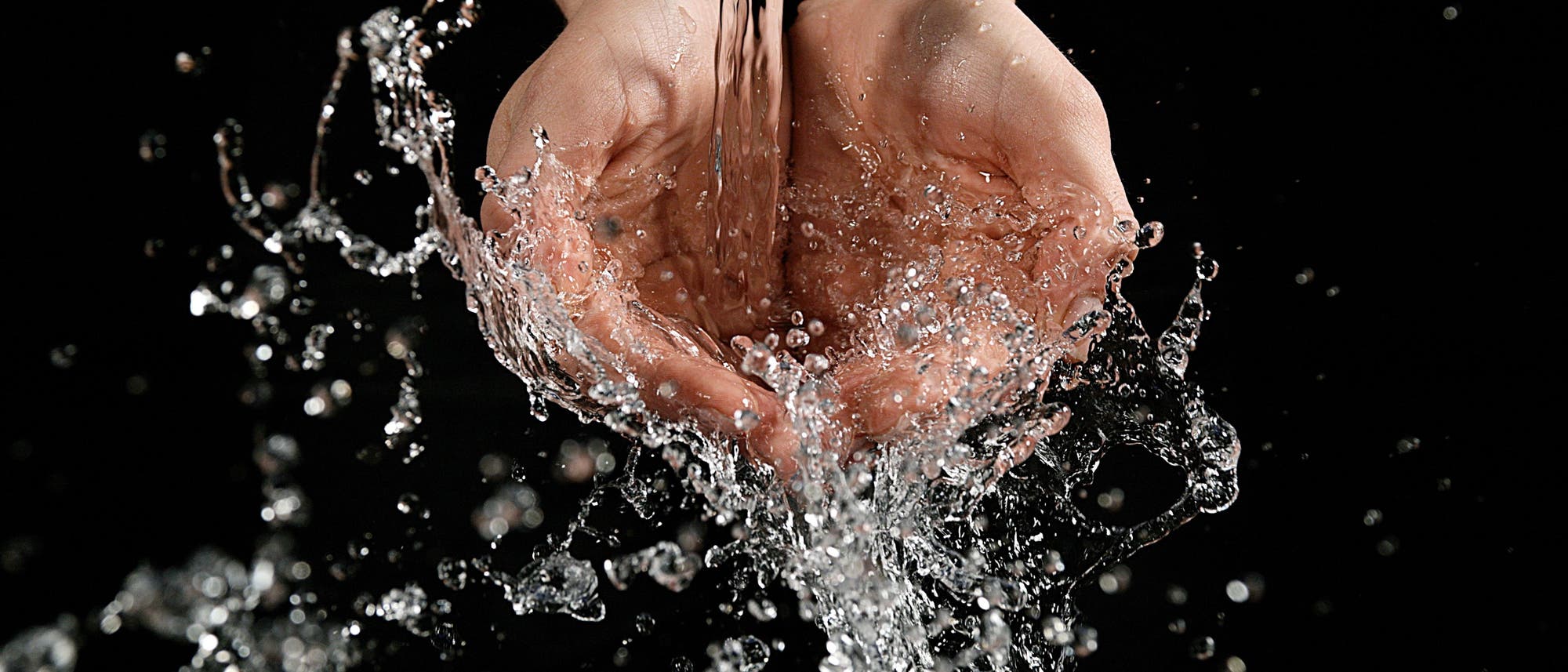 Hände vor schwarzem Hintergrund werden aus einem Wasserhahn mit Wasser begossen