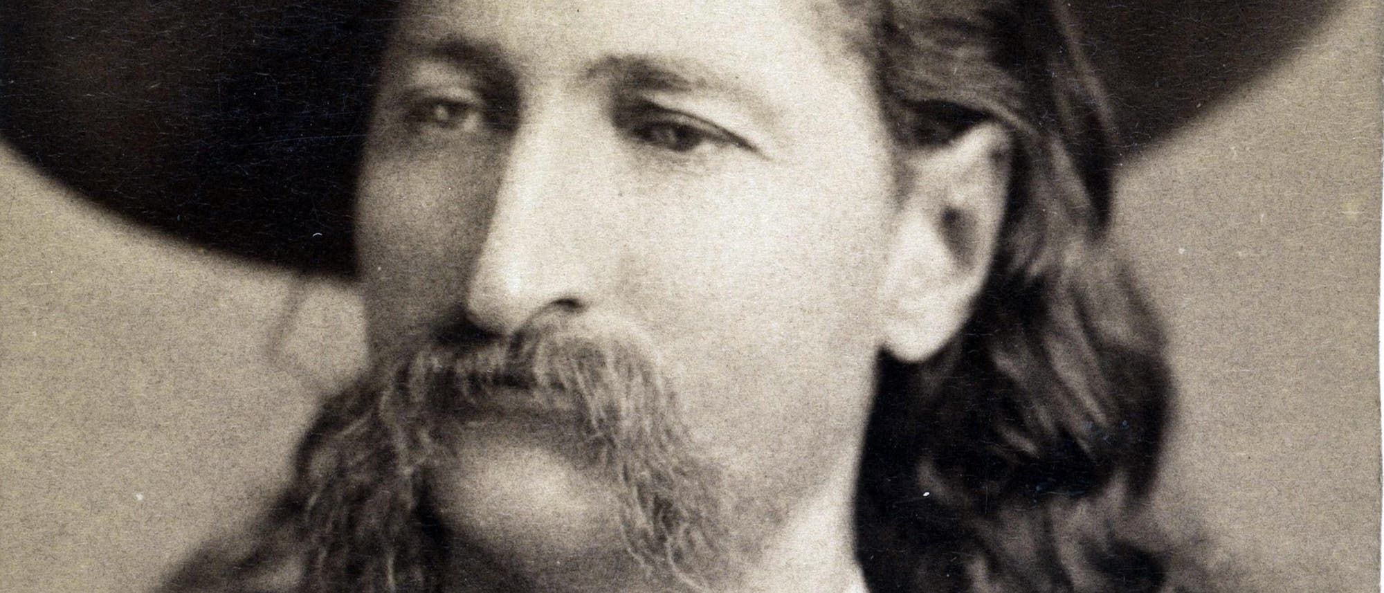 Ein historisches Schwarz-Weiß-Foto zeigt eine Person mit einem großen Hut und einem markanten Schnurrbart. Die Person blickt leicht zur Seite. Das Bild hat einen sepiafarbenen Ton, der ihm ein antikes Aussehen verleiht. Ein historisches Schwarz-Weiß-Foto zeigt eine Person mit einem großen Hut und einem markanten Schnurrbart. Die Person blickt leicht zur Seite. Das Bild hat einen sepiafarbenen Ton, der ihm ein antikes Aussehen verleiht.