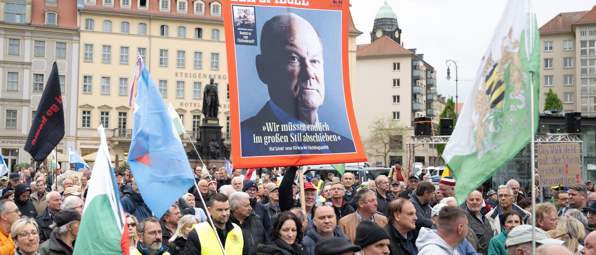 Eine Menschenmenge mit Fahnen und einem Plakat mit einer Titelseite des Nachrichtenmagazins »Der Spiegel«, das Bundeskanzler Olaf Scholz zeigt, stehen auf dem Kölner Neumarkt