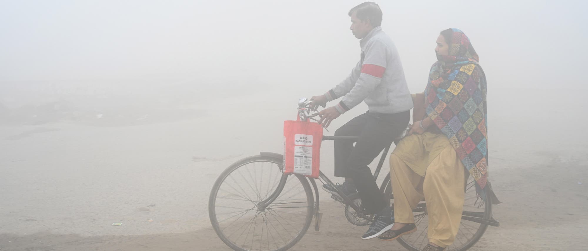 Ein Mann und eine Frau fahren auf einem Fahrrad durch den Smog in Indien