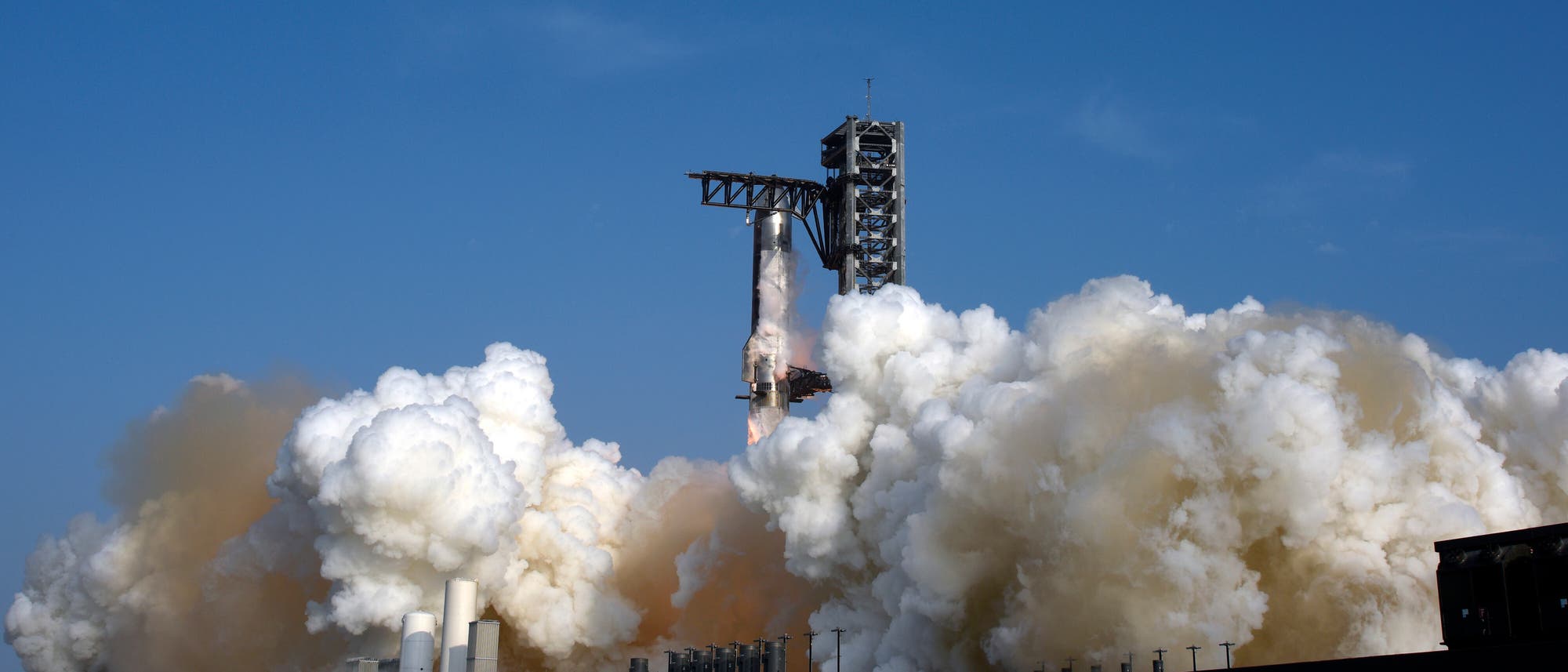 Eine Rakete hebt von einer Startrampe ab, umgeben von dichten Rauchwolken und Dampf, die in den blauen Himmel aufsteigen. Die Startrampe ist mit technischen Strukturen ausgestattet, die den Start unterstützen. Eine Rakete hebt von einer Startrampe ab, umgeben von dichten Rauchwolken und Dampf, die in den blauen Himmel aufsteigen. Die Startrampe ist mit technischen Strukturen ausgestattet, die den Start unterstützen.