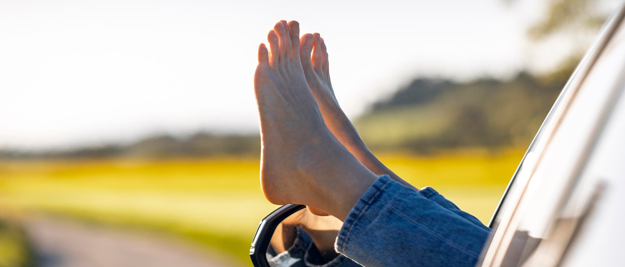 Ein Paar Beine in blauen Jeans ragt aus dem Fenster eines Autos, das auf einer ländlichen Straße fährt. Die Umgebung ist grün und sonnig, was eine entspannte und sommerliche Atmosphäre vermittelt. Im Bild ist ein Wasserzeichen mit dem Text "dpa picture alliance" sichtbar. Ein Paar Beine in blauen Jeans ragt aus dem Fenster eines Autos, das auf einer ländlichen Straße fährt. Die Umgebung ist grün und sonnig, was eine entspannte und sommerliche Atmosphäre vermittelt. Im Bild ist ein Wasserzeichen mit dem Text "dpa picture alliance" sichtbar.