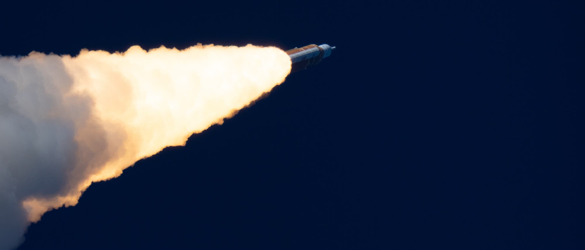 Eine Rakete steigt in den Nachthimmel auf, wobei ein heller Feuerschweif aus den Triebwerken sichtbar ist. Der Hintergrund ist dunkelblau, was den Kontrast zur leuchtenden Flamme verst&auml;rkt.