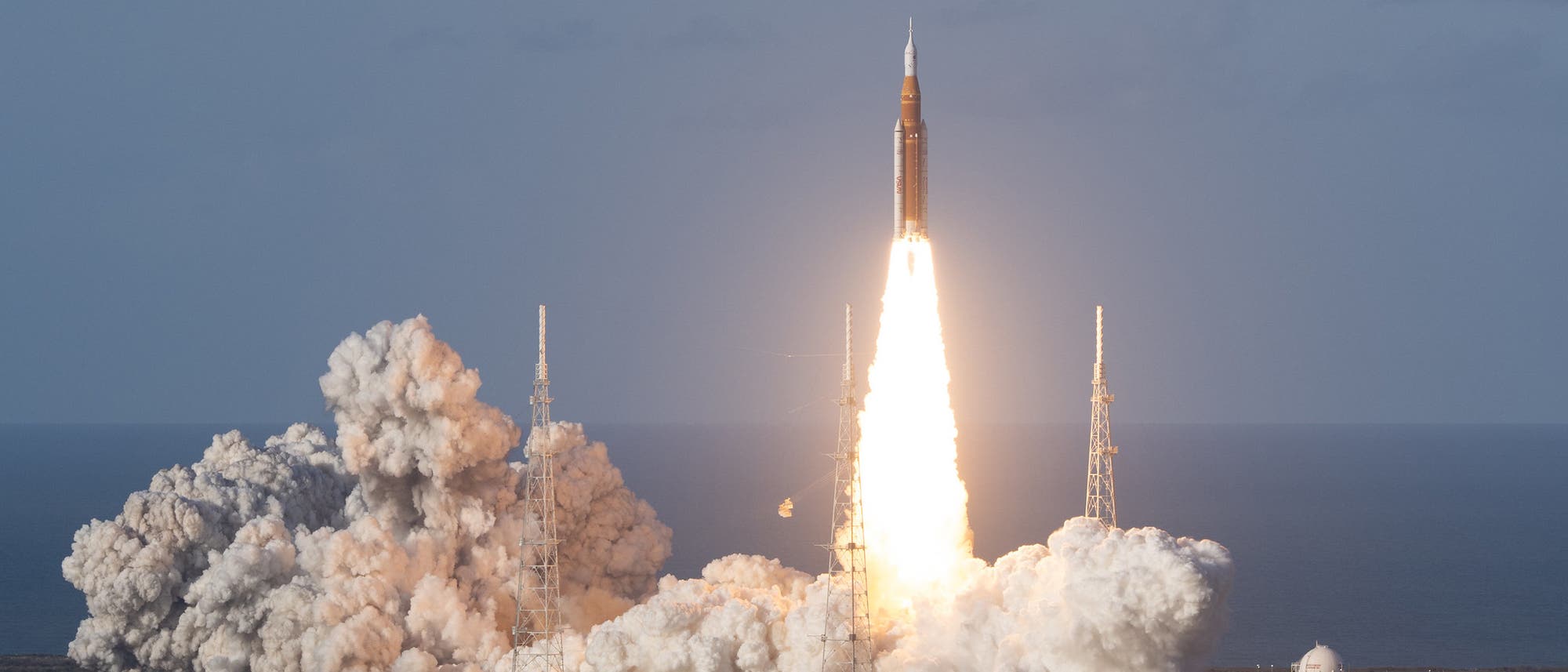 Die SLS-Rakete startet in den blauen Himmel, hinterl&auml;sst eine helle Flamme und eine Rauchspur.
