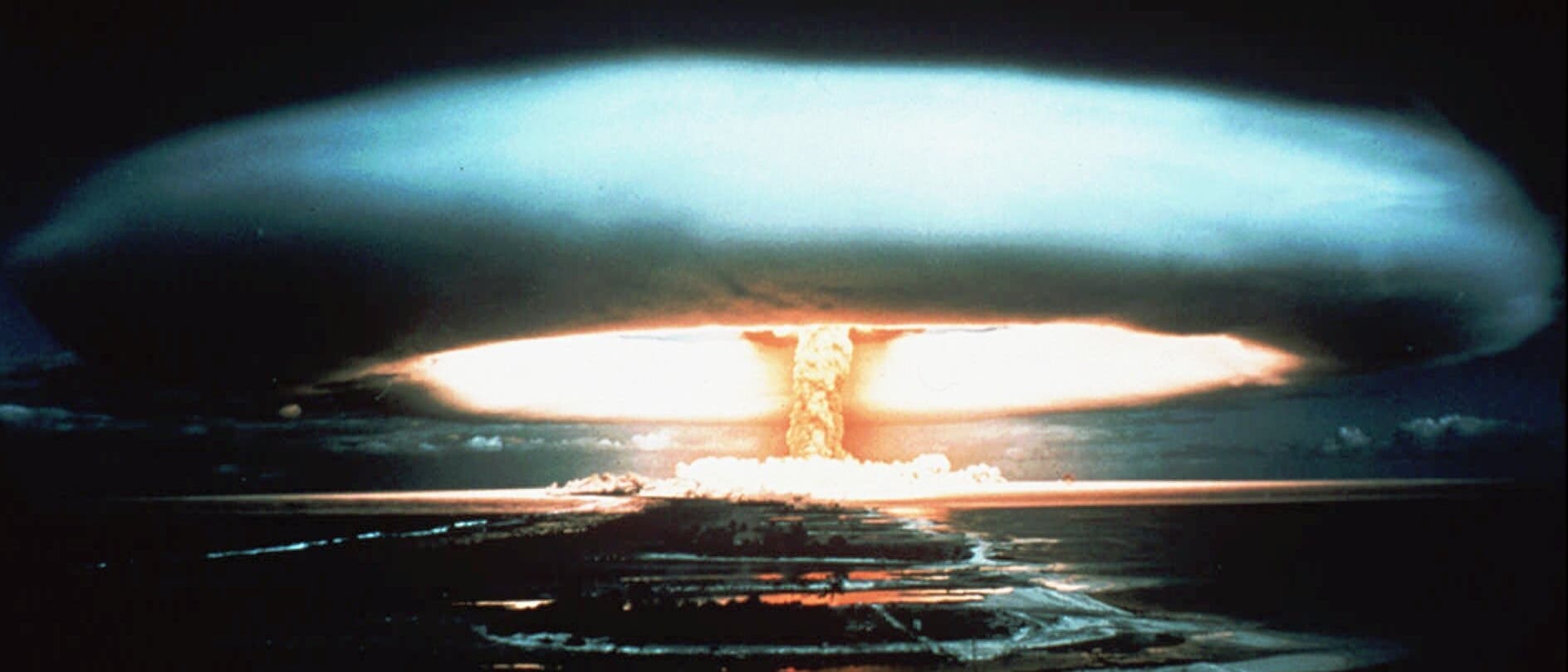 Eine große Explosion einer Atombome erzeugt einen charakteristischen Pilzwolken-Effekt über einer Landschaft. Der Himmel ist dunkel, während die Wolke in der Mitte hell erleuchtet ist, was auf die Intensität der Explosion hinweist. Die Umgebung ist flach und spiegelt das Licht der Explosion wider. Eine große Explosion einer Atombome erzeugt einen charakteristischen Pilzwolken-Effekt über einer Landschaft. Der Himmel ist dunkel, während die Wolke in der Mitte hell erleuchtet ist, was auf die Intensität der Explosion hinweist. Die Umgebung ist flach und spiegelt das Licht der Explosion wider.