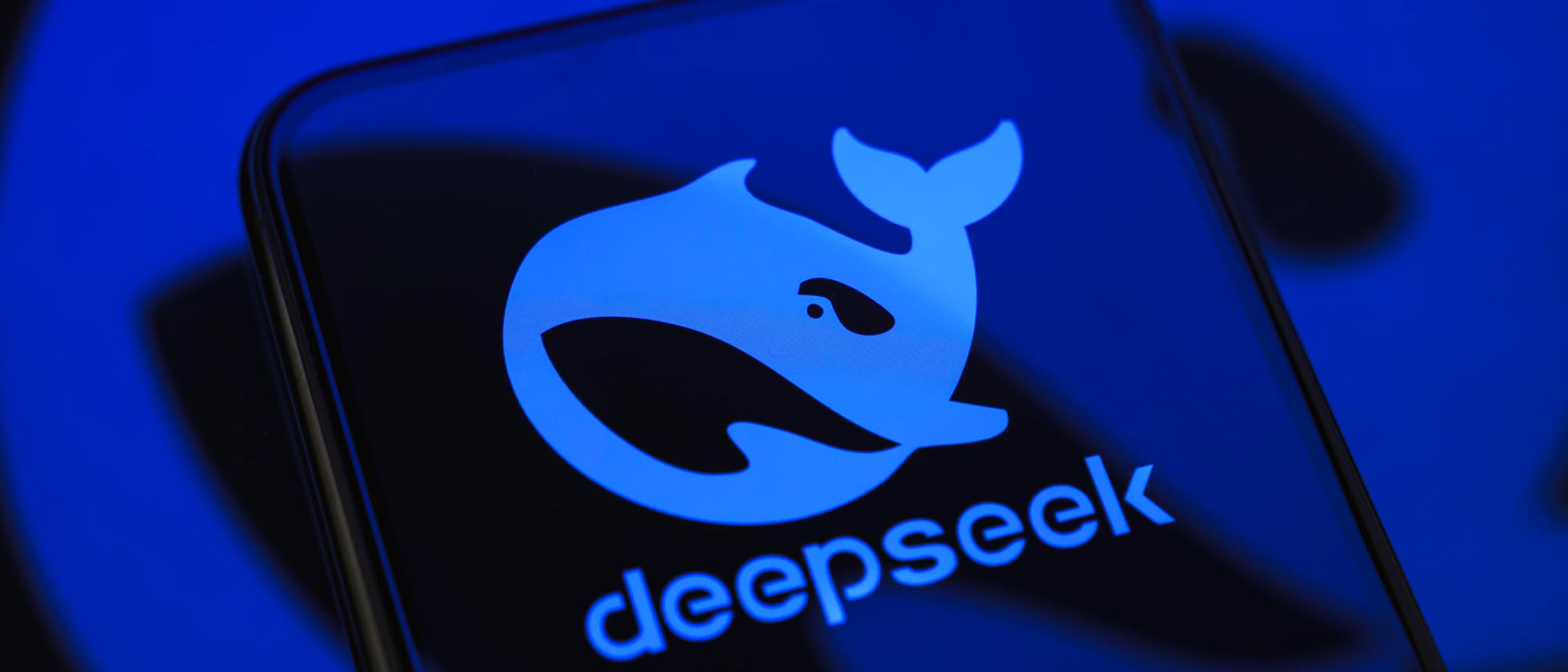Ein Smartphone-Bildschirm zeigt ein stilisiertes Wal-Symbol in Blau, begleitet vom Text &bdquo;deepseek&ldquo;. Der Hintergrund ist ebenfalls in Blau gehalten, was dem Bild einen einheitlichen, modernen Look verleiht. Das Symbol und der Text deuten auf eine Marke oder Anwendung hin, die m&ouml;glicherweise mit Technologie oder Meeresforschung in Verbindung steht.