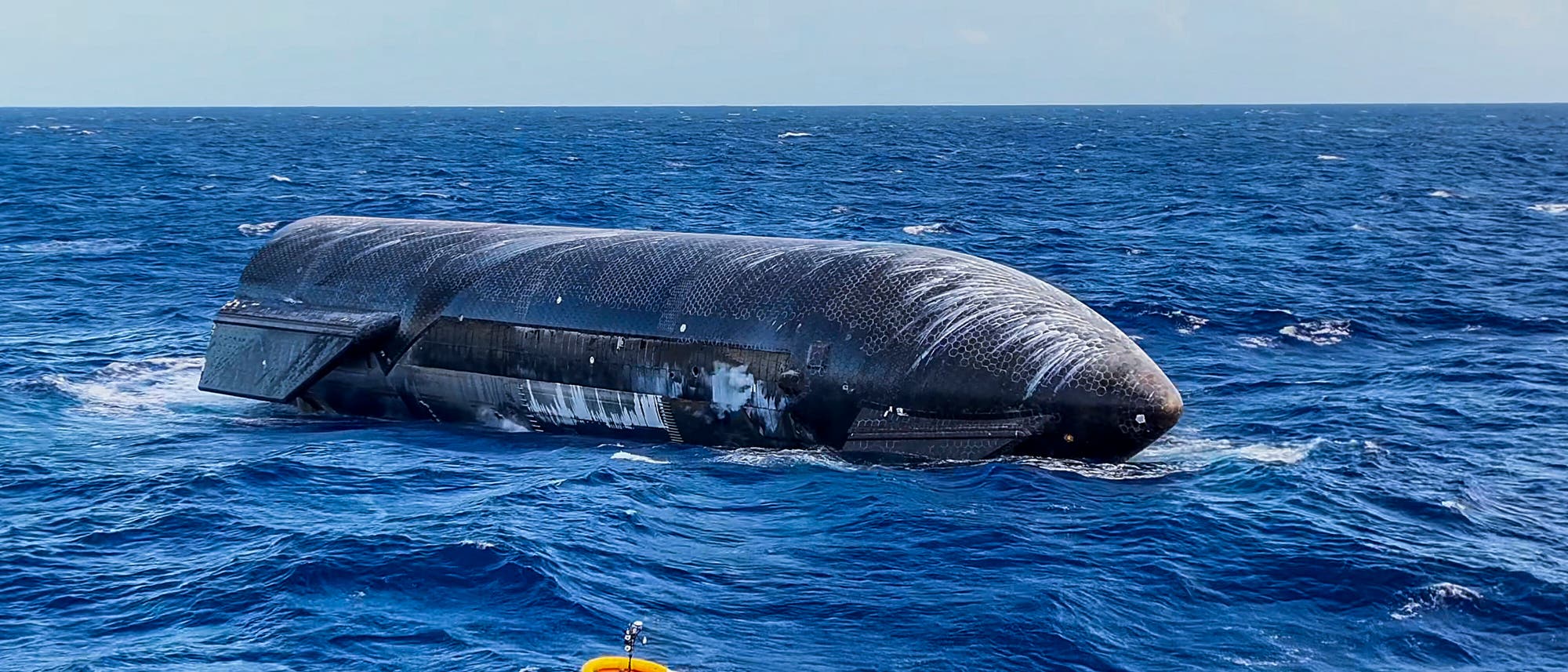 Ein Starship von SpaceX treibt im offenen Meer. Im Vordergrund schwimmt eine orangefarbene Boje auf den Wellen. Der Himmel ist klar und blau. Das Wasser ist tiefblau und leicht bewegt. Ein Starship von SpaceX treibt im offenen Meer. Im Vordergrund schwimmt eine orangefarbene Boje auf den Wellen. Der Himmel ist klar und blau. Das Wasser ist tiefblau und leicht bewegt.