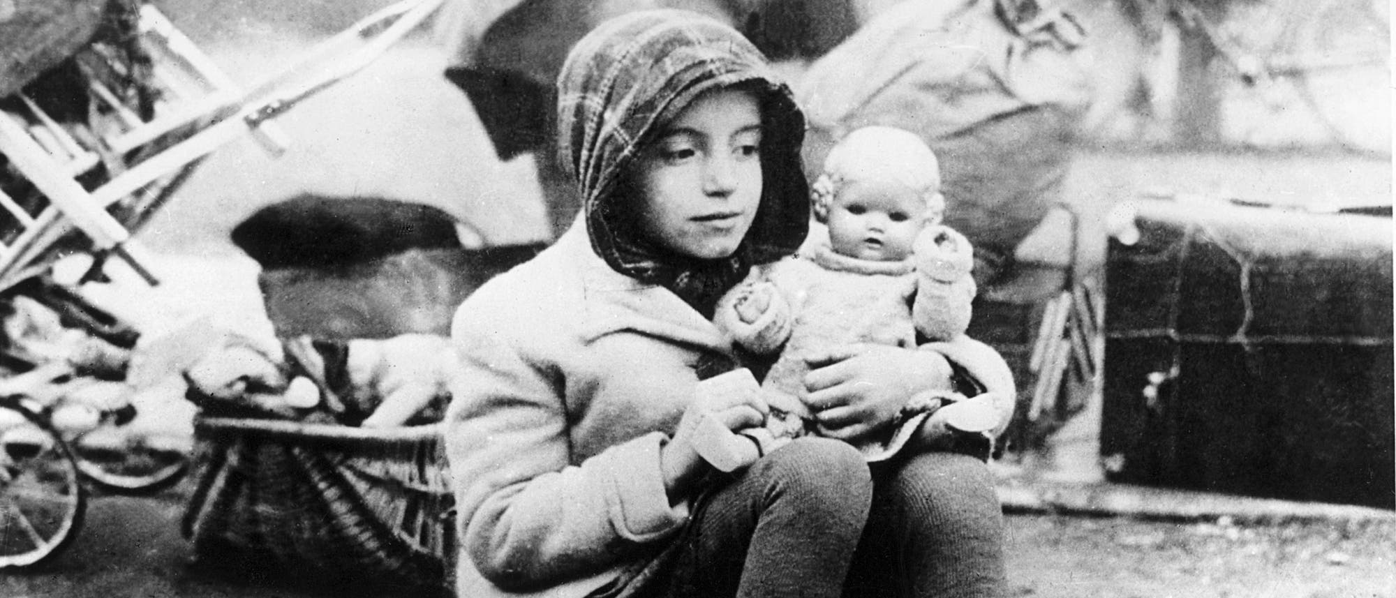 Ein Mädchen, das zu einem Flüchtlingstreck in der Nachkriegszeit gehört, hält seine Puppe im Arm.