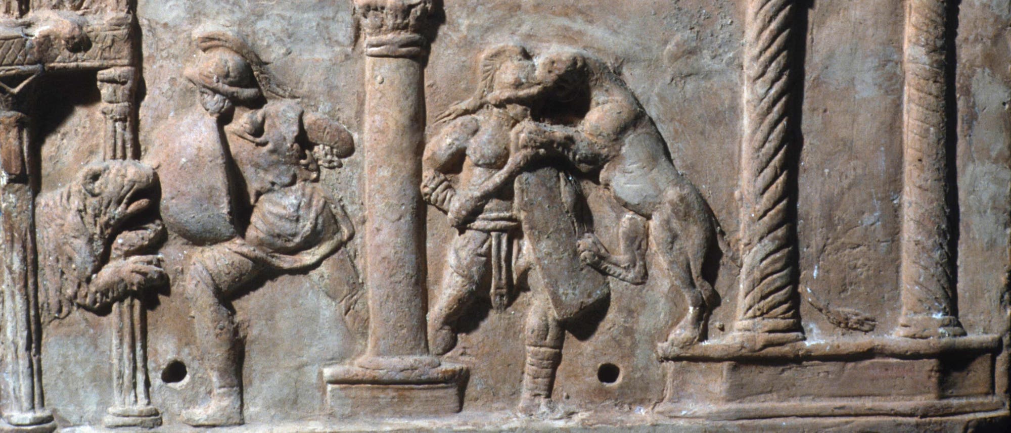 Ein antikes römisches Relief zeigt eine Szene mit mehreren Figuren. Es ist eine Arena mit Säulen zu sehen, in der zwei Gladiatoren mit wilden Tieren kämpfen. Ein antikes römisches Relief zeigt eine Szene mit mehreren Figuren. Es ist eine Arena mit Säulen zu sehen, in der zwei Gladiatoren mit wilden Tieren kämpfen.