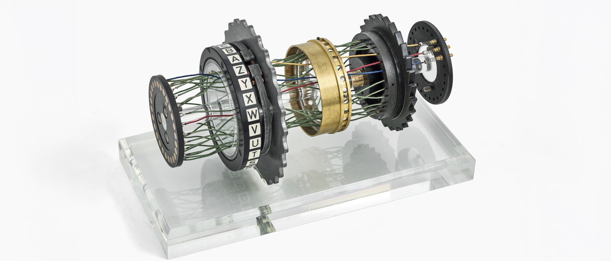 Eine 3D-Darstellung eines Teils der Enigma-Maschine, die aus mehreren rotierenden Walzen besteht. Die Walzen sind mit Buchstaben des Alphabets beschriftet und durch Dr&auml;hte verbunden. Diese Anordnung zeigt, wie die Maschine zur Verschl&uuml;sselung von Nachrichten verwendet wurde. Im Hintergrund ist ein Text &uuml;ber die Funktionsweise der Enigma-Maschine zu sehen, der die polyalphabetische Substitution erkl&auml;rt.