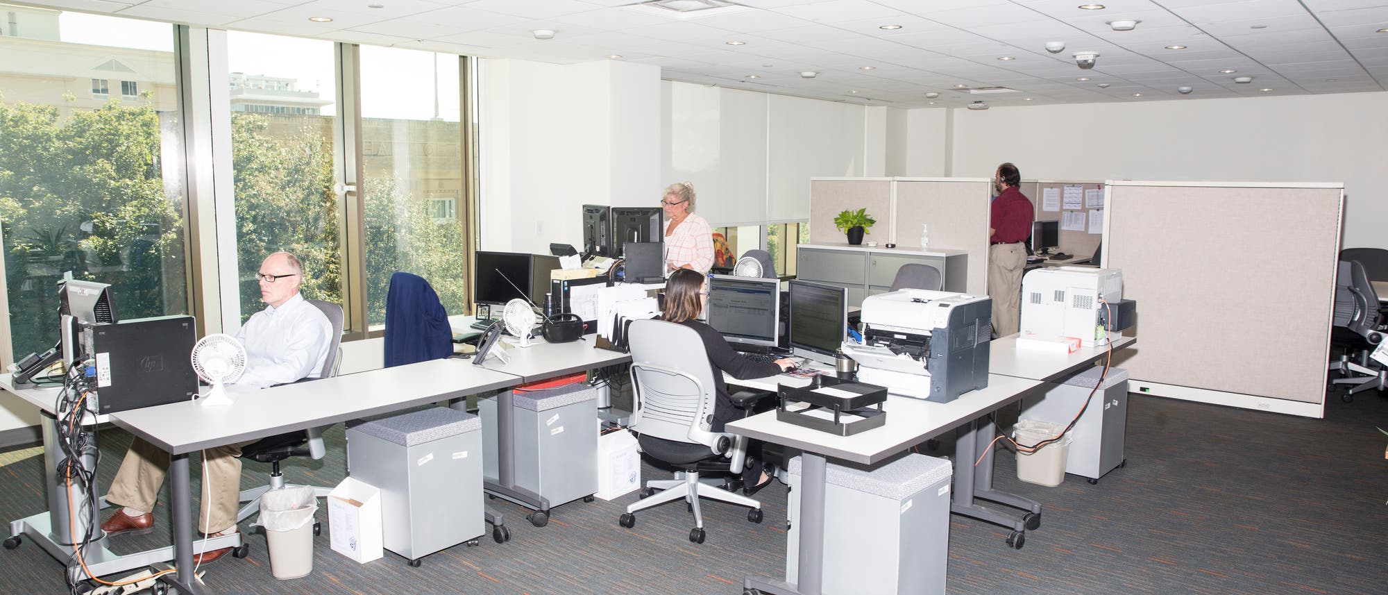 Ein Büroraum mit mehreren Tischen, auf denen sich diverse Büromaterialien und ein Computermonitor befinden.