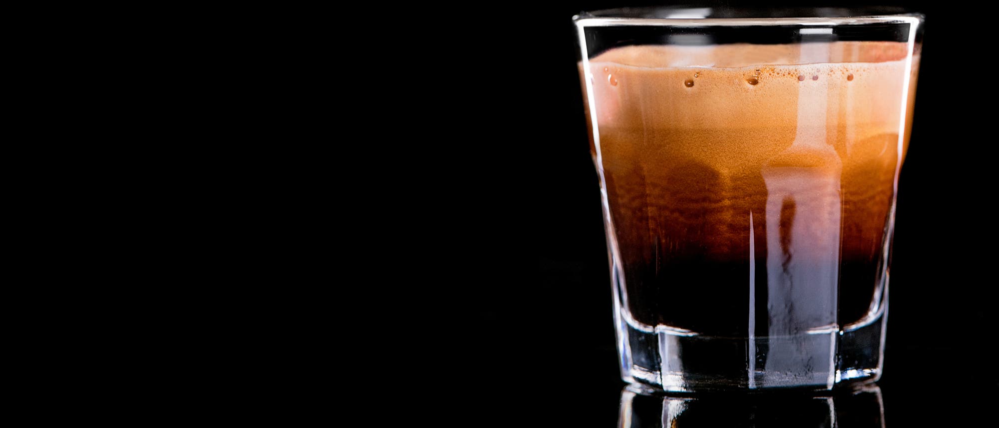 Ein durchsichtiges Glas mit einem dunklen Espresso, dessen Crema sich gerade noch setzt.
