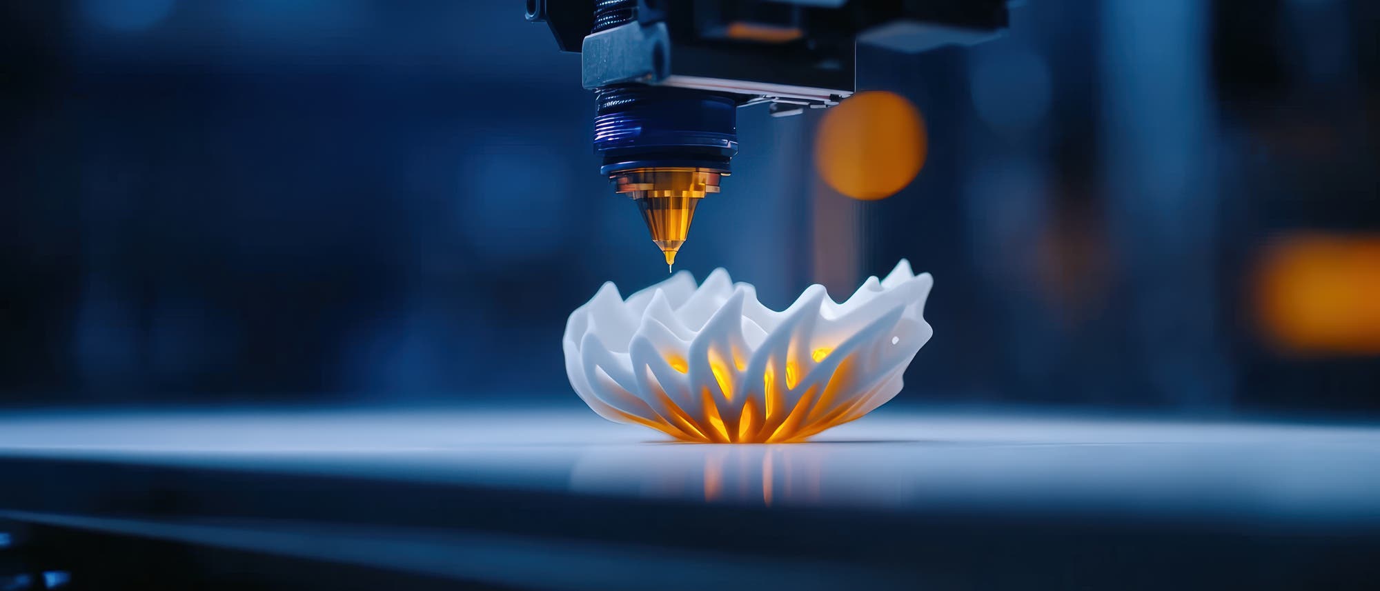 Ein 3-D-Drucker erstellt ein komplexes, blütenförmiges Objekt aus weißem Material. Der Druckkopf ist in Aktion zu sehen, während das Objekt auf einer glatten Oberfläche liegt. Die Szene ist in einem blauen Licht gehalten, das dem Bild eine futuristische Atmosphäre verleiht. Im Hintergrund sind unscharfe Lichter zu erkennen.