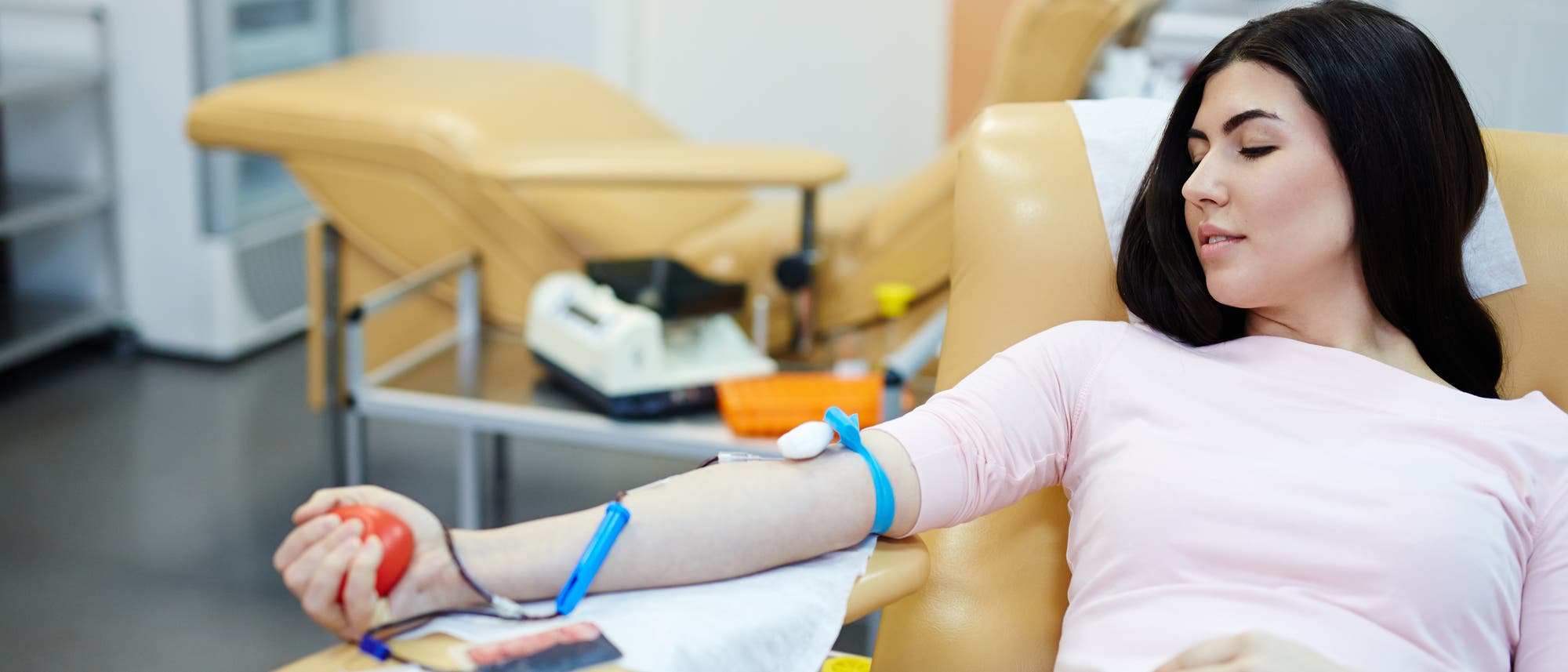 Eine junge Frau sitzt in einem Sessel und spendet Blut in einer Art medizinischem Zentrum.