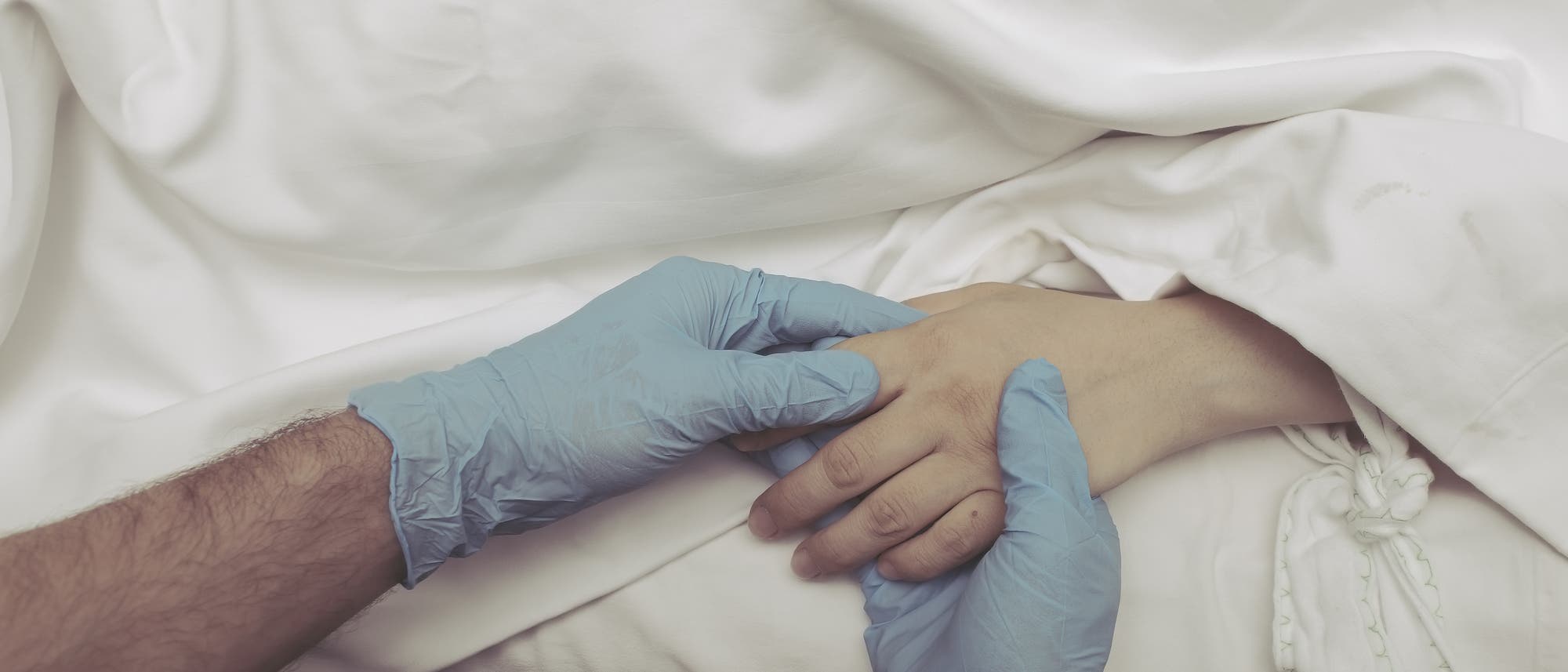 Eine Hand mit typischen Krankenhaus-Einmalhandschuhen hält die Hand eines Patienten.
