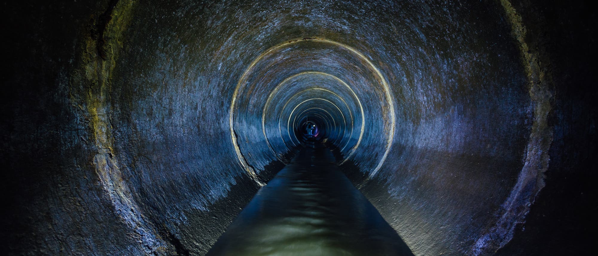 Ein Blick in einen lang gestreckten, dunklen Kanalisationstunnel