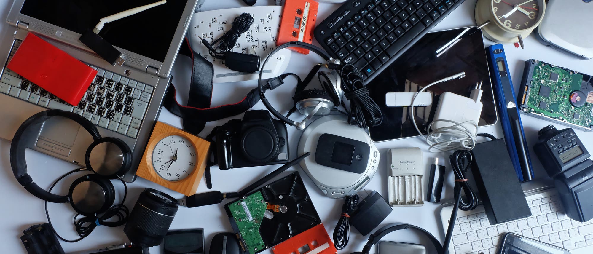Eine Vielzahl von elektronischen Geräten und Zubehörteilen, darunter ein Laptop, eine Tastatur, Kopfhörer, eine Kamera, ein Taschenrechner, ein Wecker, ein Telefon, Batterien und verschiedene Kabel, sind auf einer weißen Oberfläche verstreut. Die Anordnung zeigt eine Mischung aus alten und neuen Technologien, die den Fortschritt und die Vielfalt in der Elektronik veranschaulichen. Eine Vielzahl von elektronischen Geräten und Zubehörteilen, darunter ein Laptop, eine Tastatur, Kopfhörer, eine Kamera, ein Taschenrechner, ein Wecker, ein Telefon, Batterien und verschiedene Kabel, sind auf einer weißen Oberfläche verstreut. Die Anordnung zeigt eine Mischung aus alten und neuen Technologien, die den Fortschritt und die Vielfalt in der Elektronik veranschaulichen.