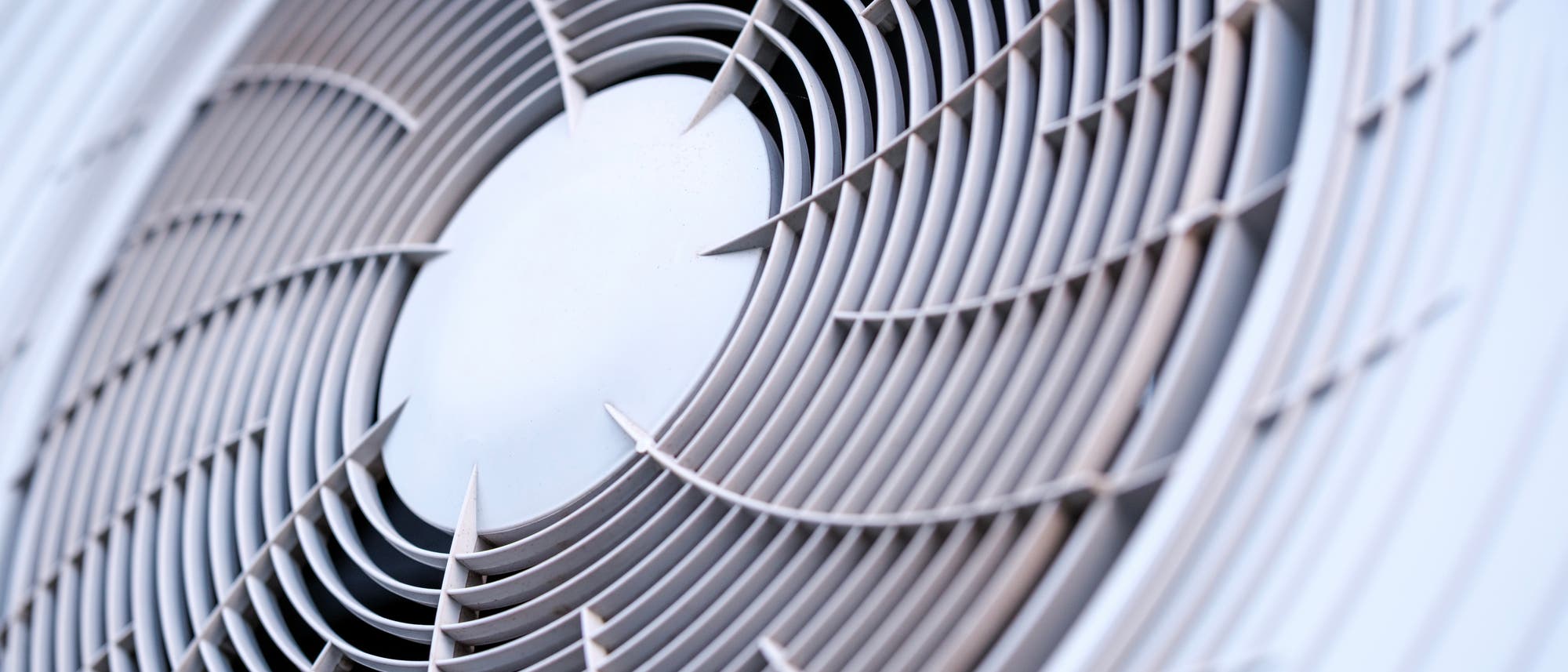 Nahaufnahme eines L&uuml;ftungsgitters einer Klimaanlage. Die konzentrischen, gebogenen Lamellen sind symmetrisch um einen zentralen Punkt angeordnet und erzeugen ein spiralf&ouml;rmiges Muster. 