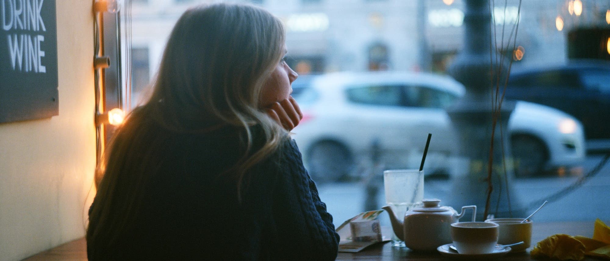 Frau allein im Café, stützt das Kinn auf die Hand und schaut aus dem Fenster.