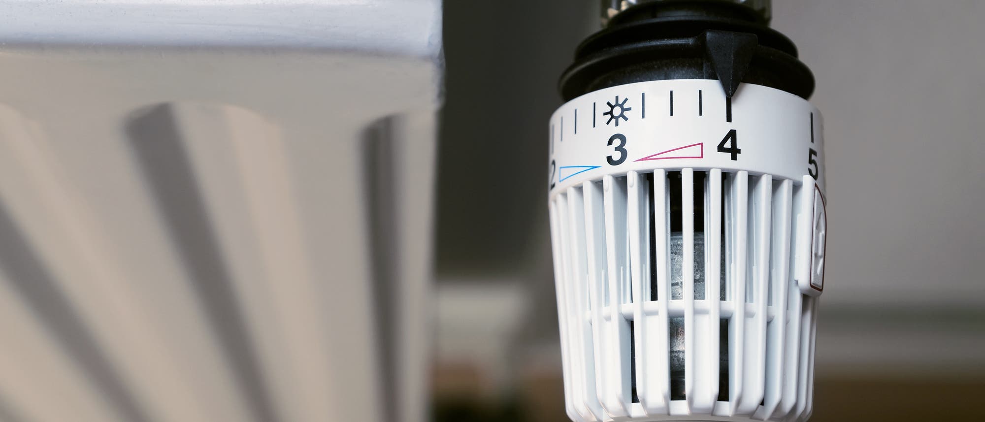 Ein Heizk&ouml;rperthermostat mit einer Skala von 1 bis 5, wobei der Regler auf Stufe 3 eingestellt ist. Das Thermostat zeigt Symbole f&uuml;r K&auml;lte und W&auml;rme an. Links im Bild ist ein Teil des Heizk&ouml;rpers sichtbar.