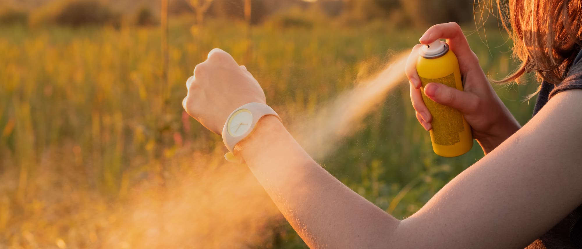Eine Person sprüht Insektenschutzmittel aus einer gelben Sprühdose großzügig auf ihren Arm. Eine Person sprüht Insektenschutzmittel aus einer gelben Sprühdose großzügig auf ihren Arm.