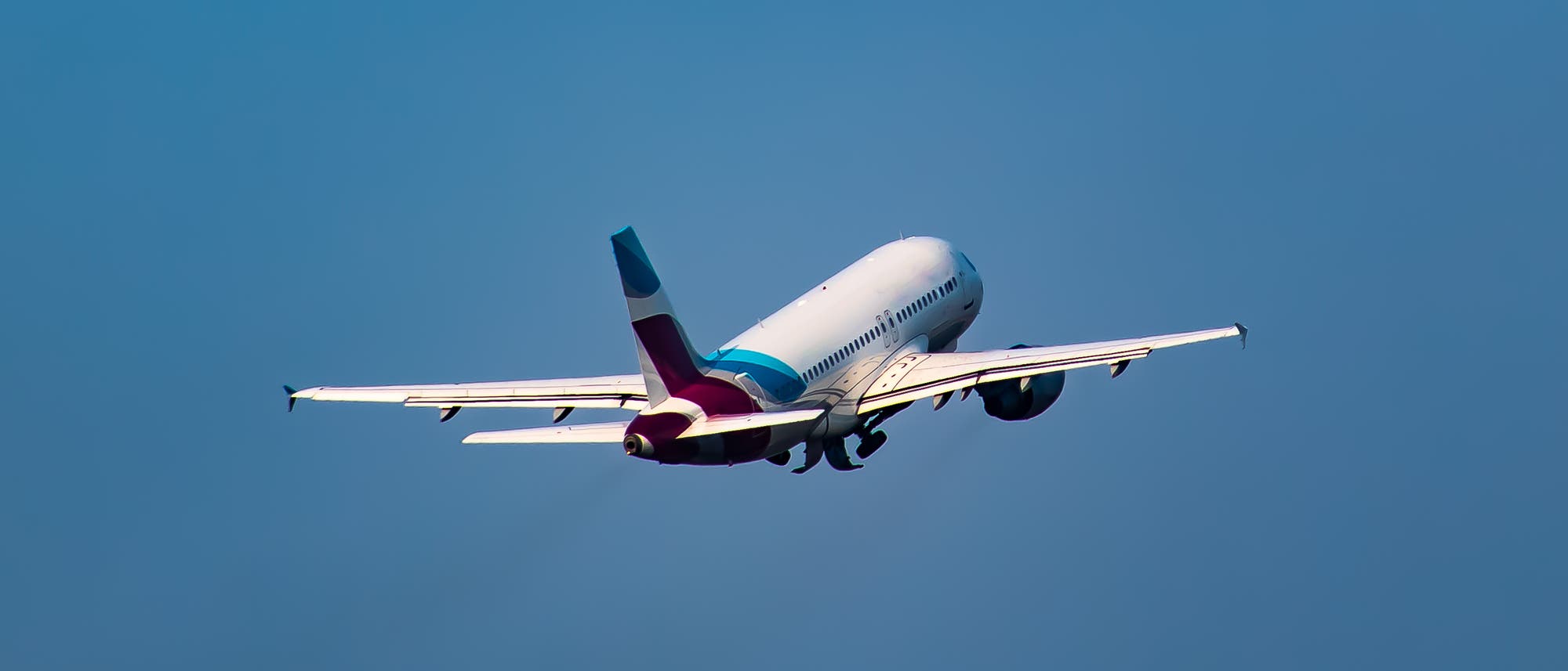 Ein Passagierflugzeug hebt in den blauen, wolkenlosen Himmel ab. Die Triebwerke sind sichtbar und das Fahrwerk wird gerade eingezogen. 