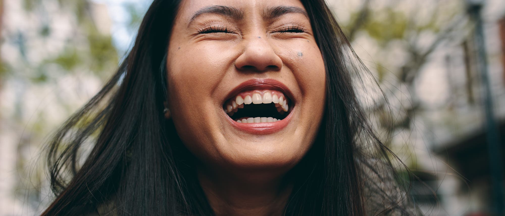 Eine Person lacht herzlich im Freien. 