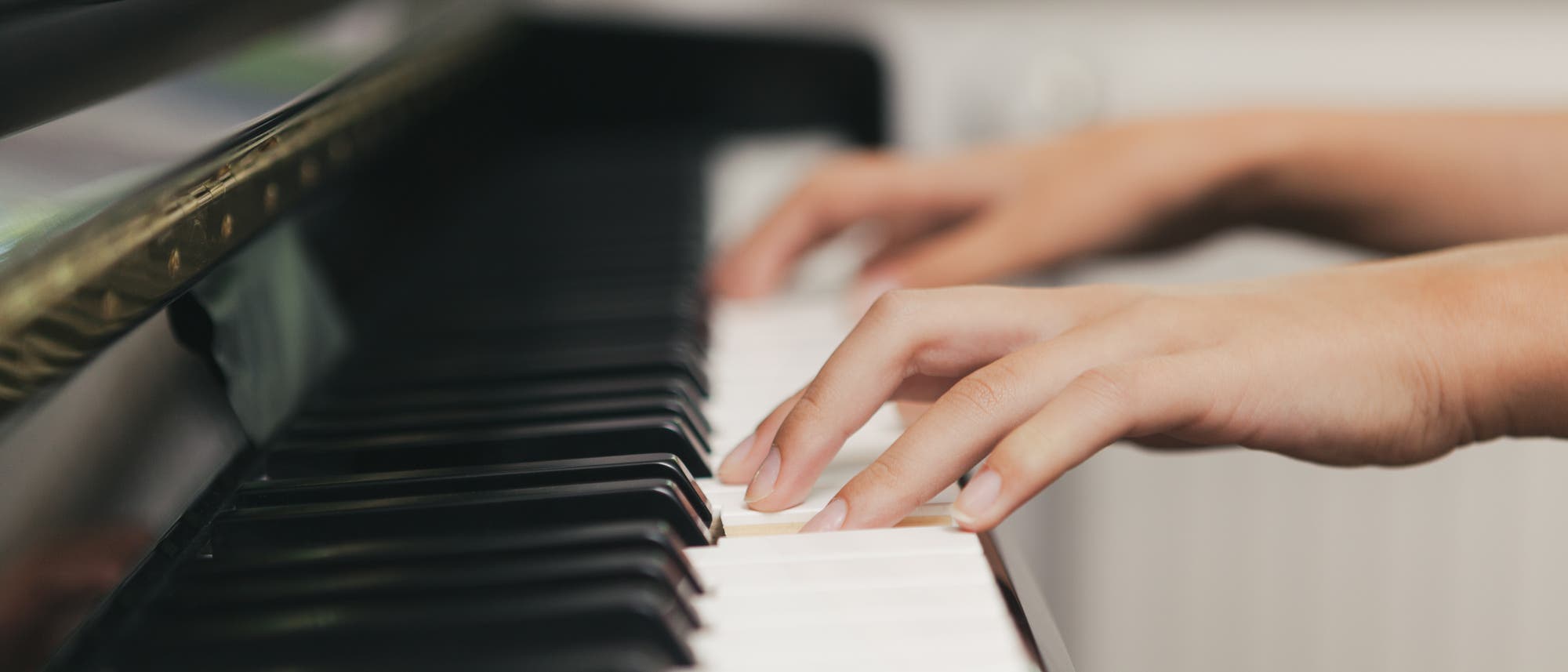 Eine Person spielt Klavier, wobei die Hände auf den Tasten ruhen. Die Nahaufnahme zeigt die Finger, die sanft auf den weißen und schwarzen Tasten positioniert sind, während das glänzende Gehäuse des Klaviers im Hintergrund sichtbar ist. Eine Person spielt Klavier, wobei die Hände auf den Tasten ruhen. Die Nahaufnahme zeigt die Finger, die sanft auf den weißen und schwarzen Tasten positioniert sind, während das glänzende Gehäuse des Klaviers im Hintergrund sichtbar ist.