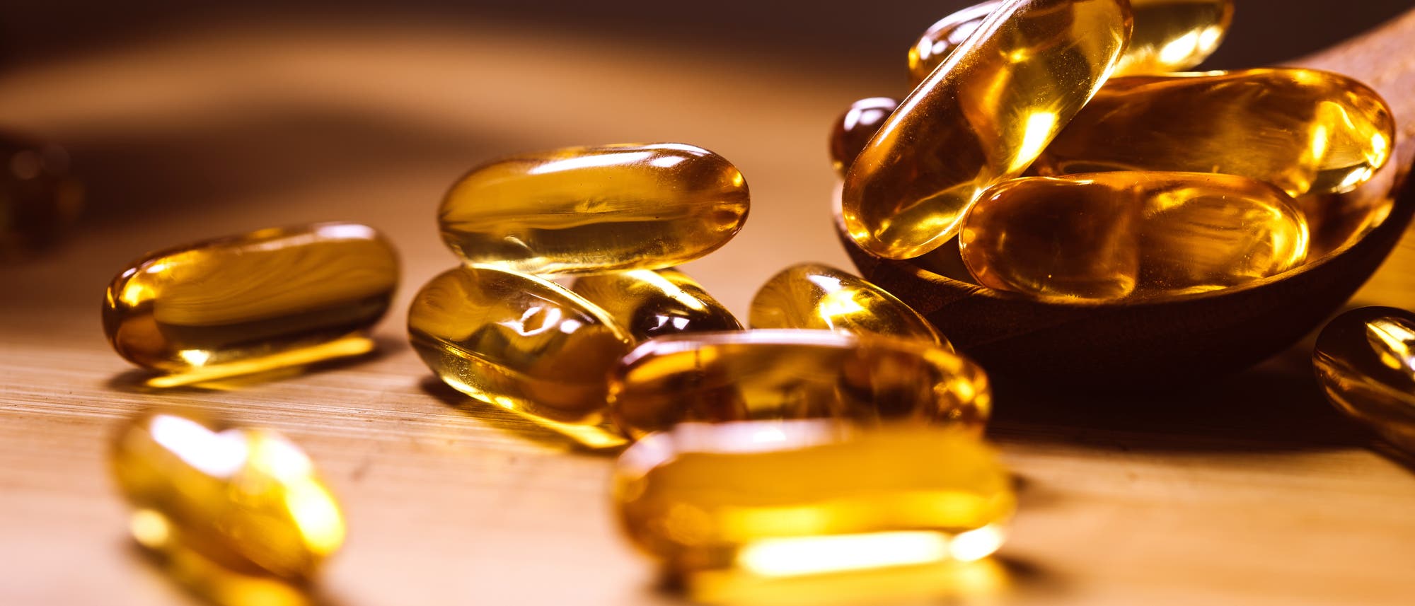 Auf einem Tisch liegen verstreut einige honigfarbene Vitamin-D-Kapseln