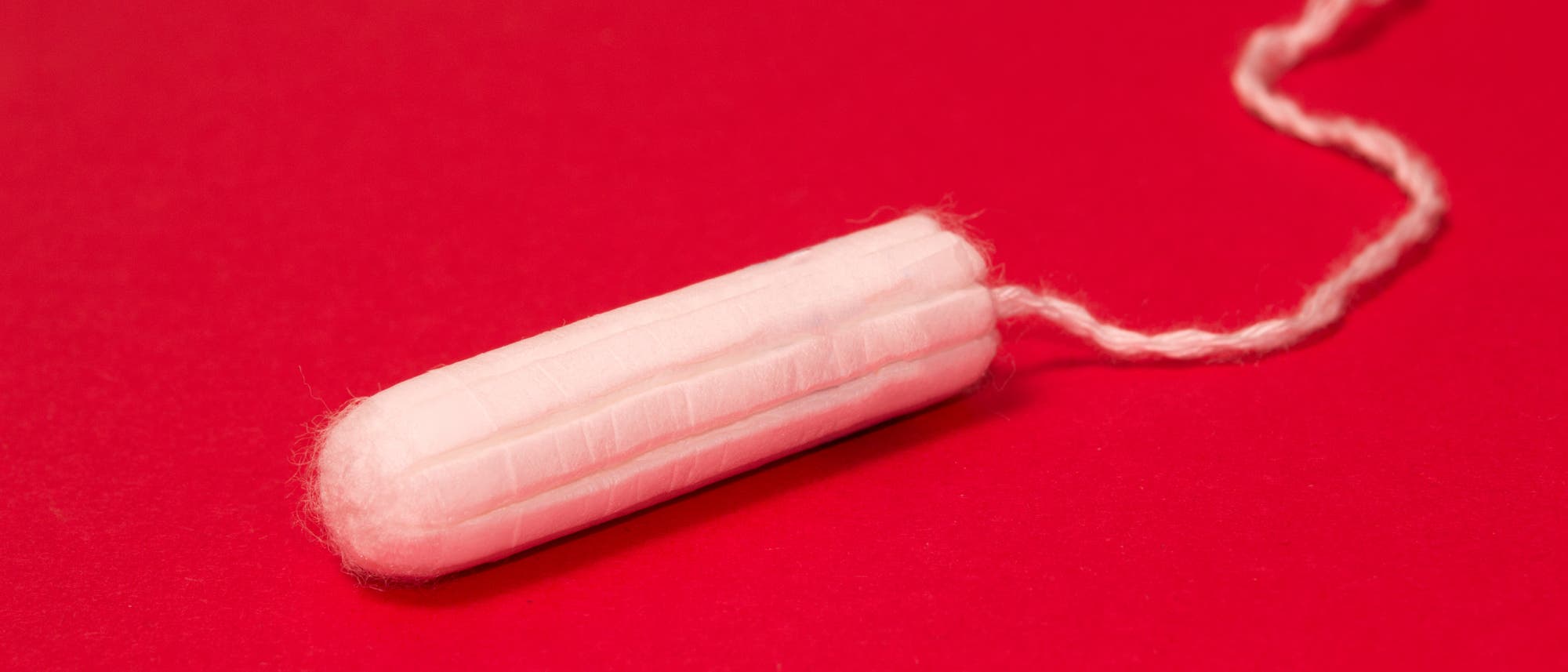 Ein weißer Tampon mit Rückholfaden liegt auf einem roten Hintergrund. Das Bild hebt die kontrastreiche Farbe hervor und betont die Hygiene und den Gebrauch von Tampons. Ein weißer Tampon mit Rückholfaden liegt auf einem roten Hintergrund. Das Bild hebt die kontrastreiche Farbe hervor und betont die Hygiene und den Gebrauch von Tampons.