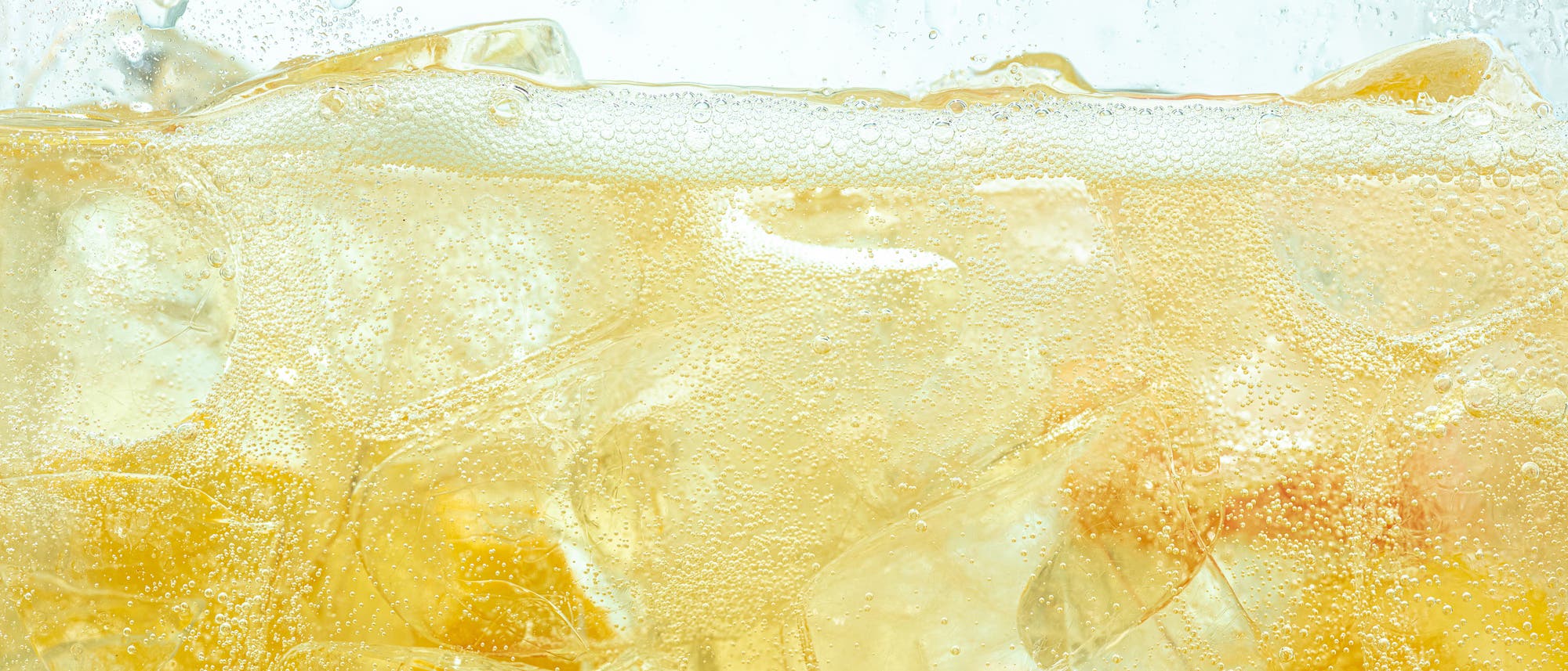 Nahaufnahme eines Glases, das mit Eisw&uuml;rfeln und Energydrink gef&uuml;llt ist. Die Kohlens&auml;ure ist als kleine Bl&auml;schen im gelben Getr&auml;nk sichtbar.