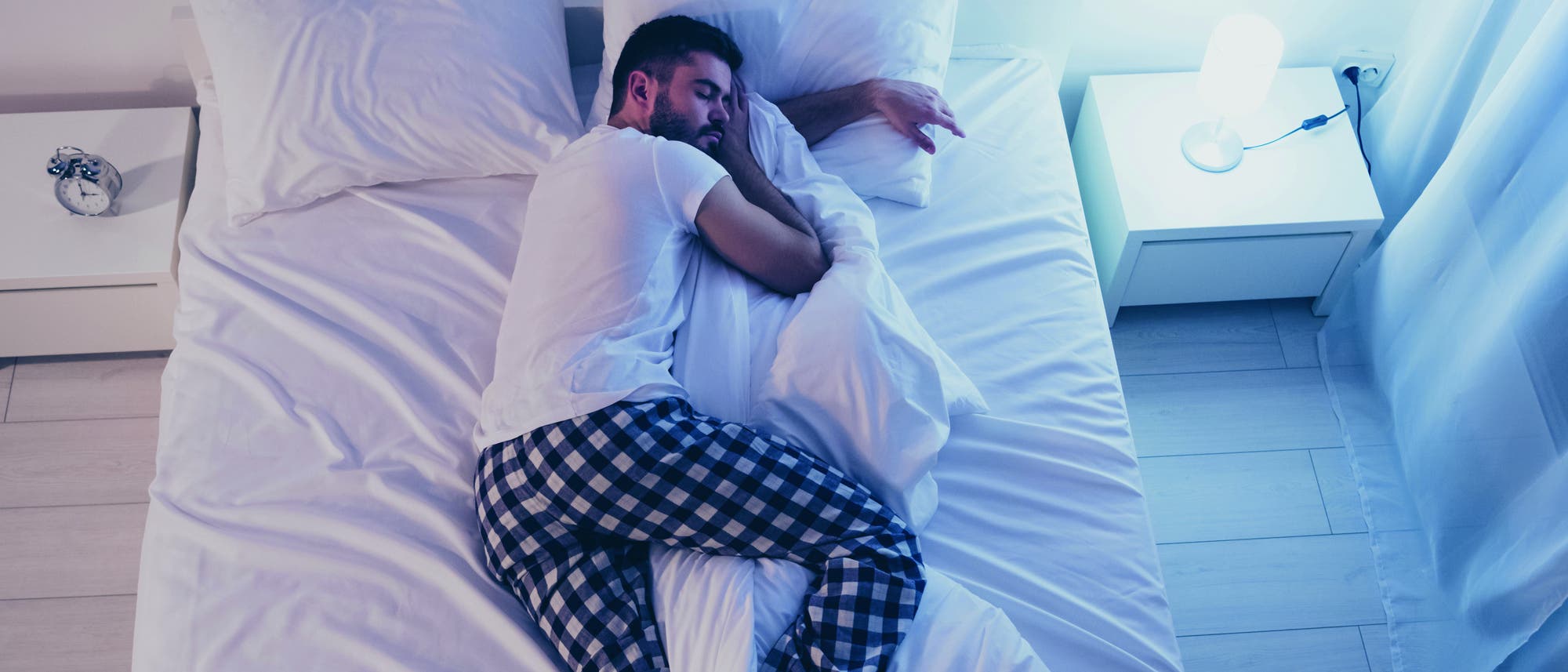Ein junger Mann liegt mit angewinkeltem Bein im Bett und schläft.